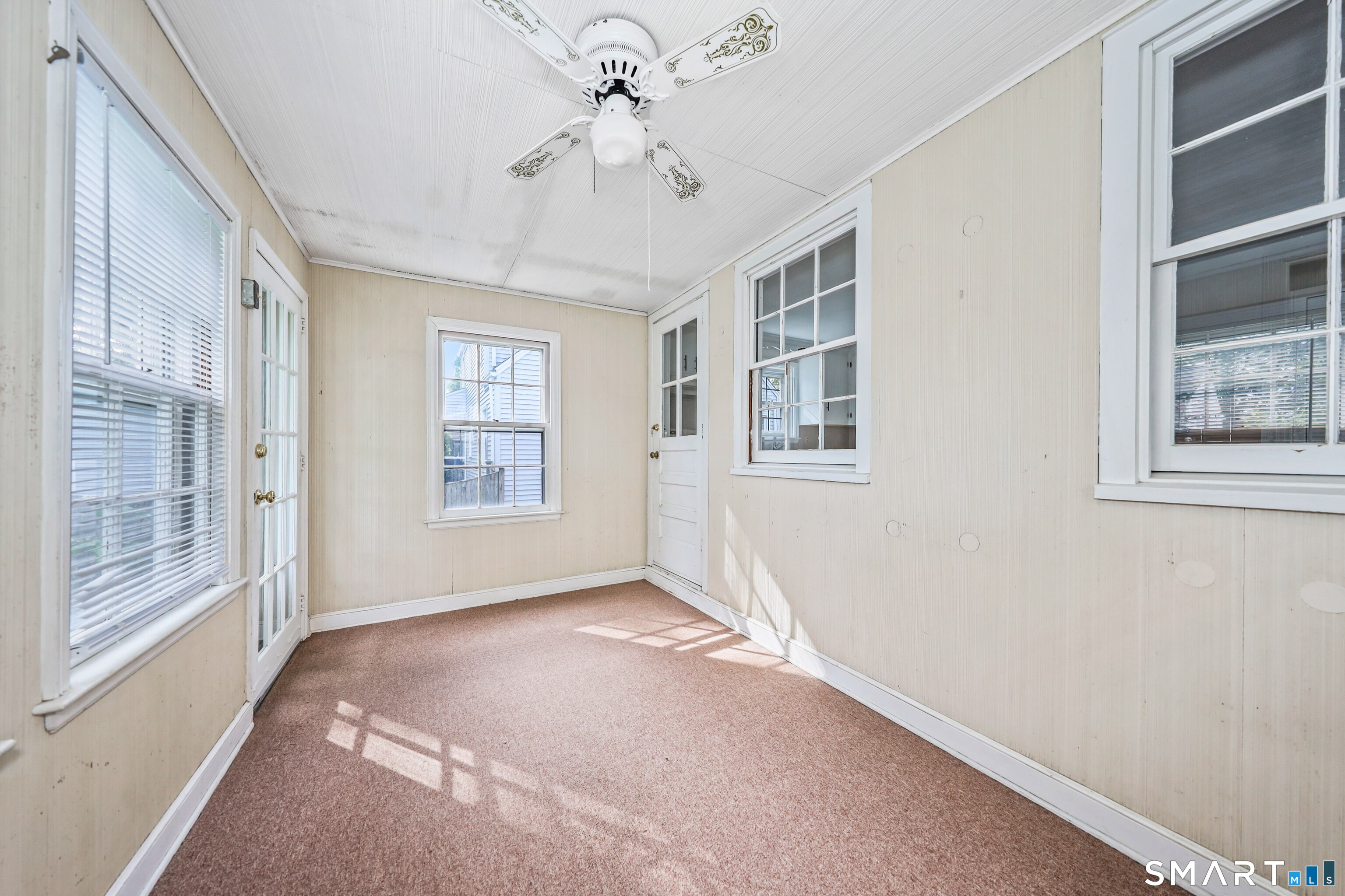 Enclosed sunroom with a decorative ceiling fan, many windows, and rose-colored carpeting.