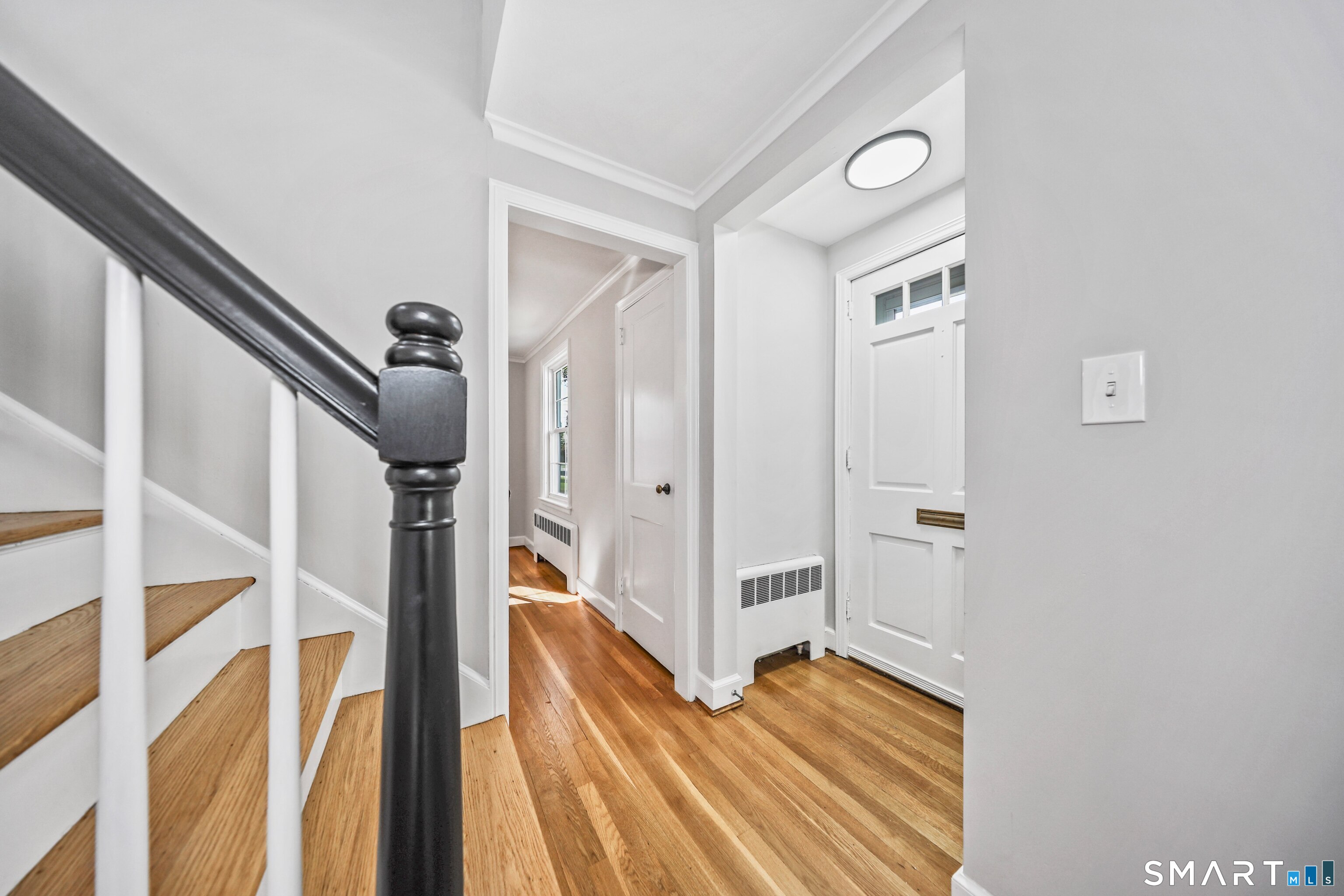 Entry hall with hardwood floors, a white front door, and a staircase with a dark handrail.
