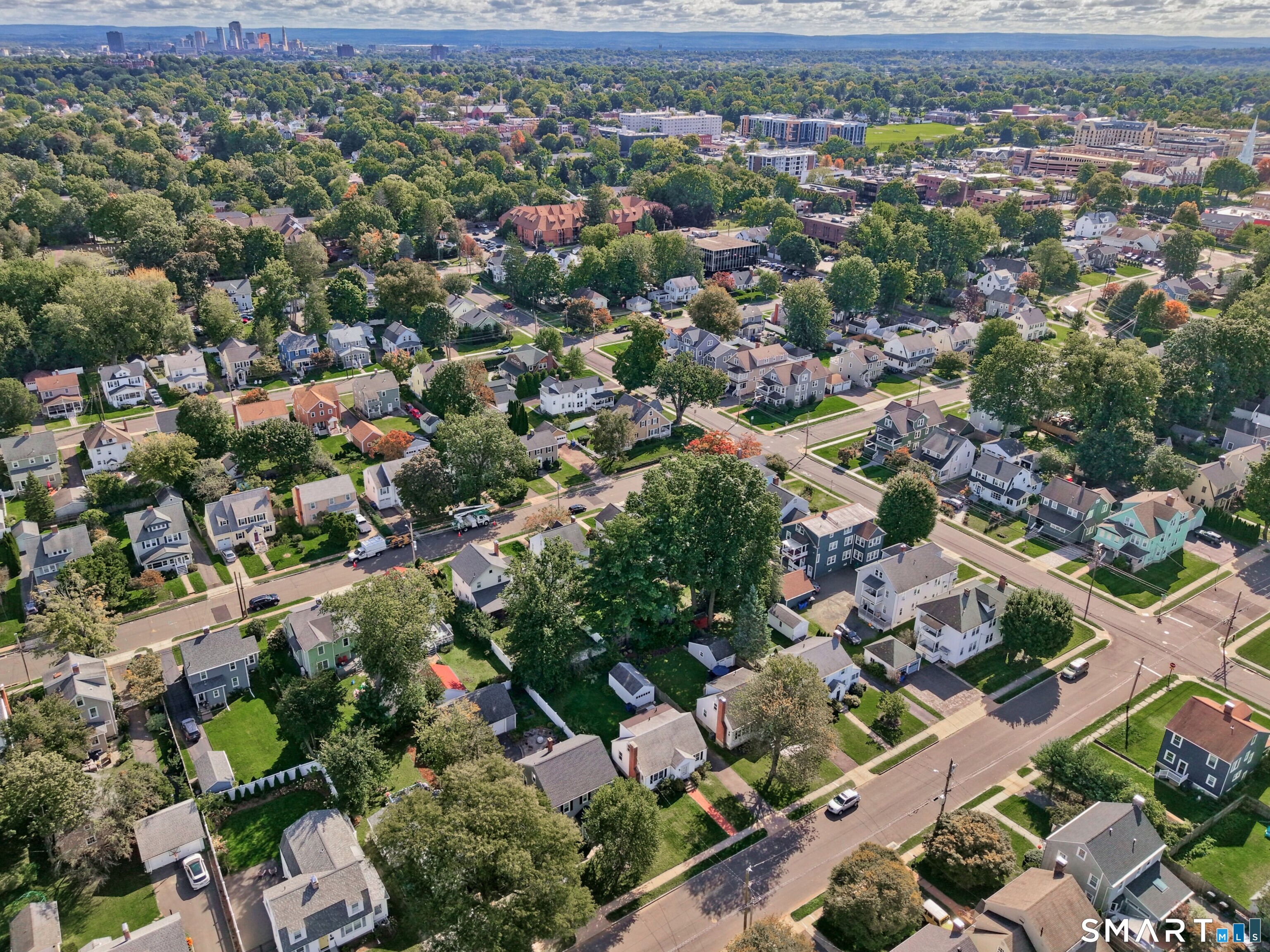 Aerial view of a tree-lined West Hartford neighborhood with homes and a distant city skyline.