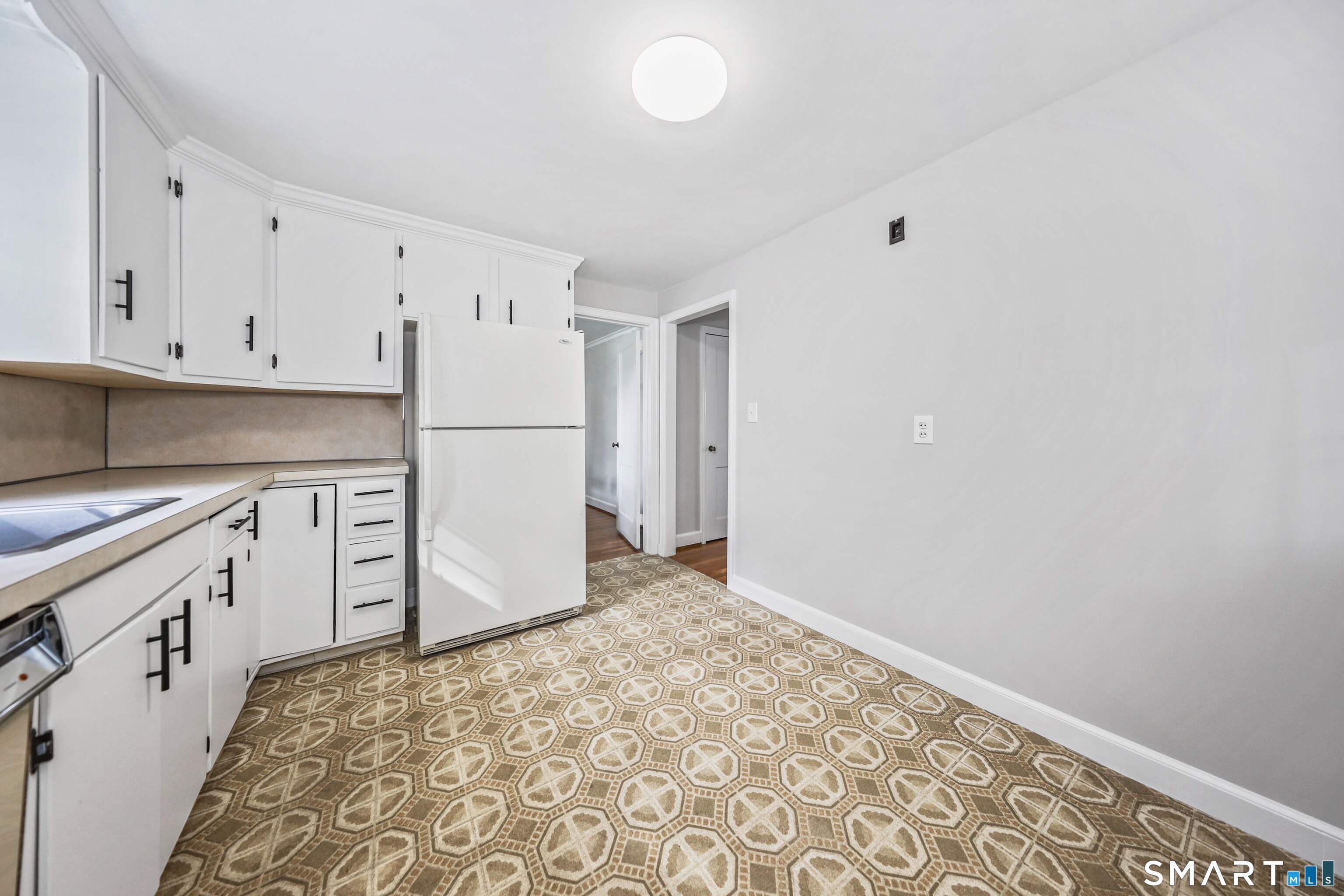 Kitchen with white cabinets and refrigerator, beige counters, and patterned brown floor.