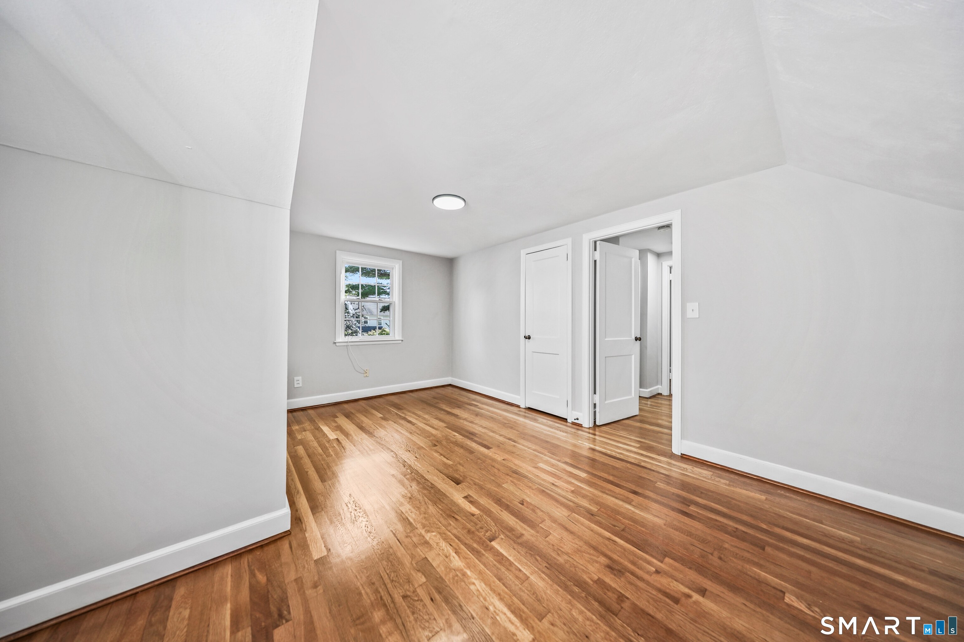Empty room with polished hardwood floors, white walls, and a small window.