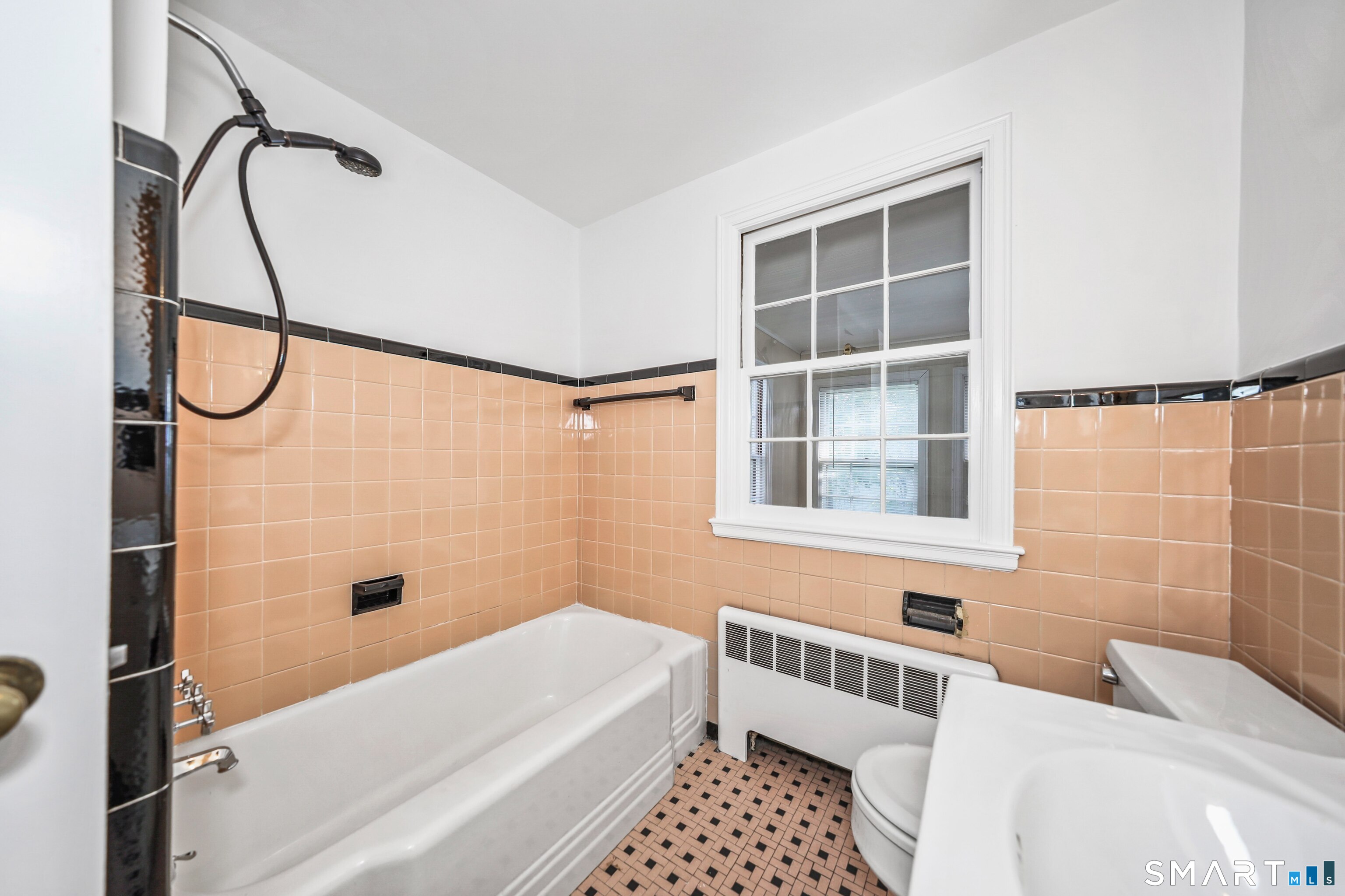 Bathroom with peach tile, a white tub and shower, mosaic floor, and window.
