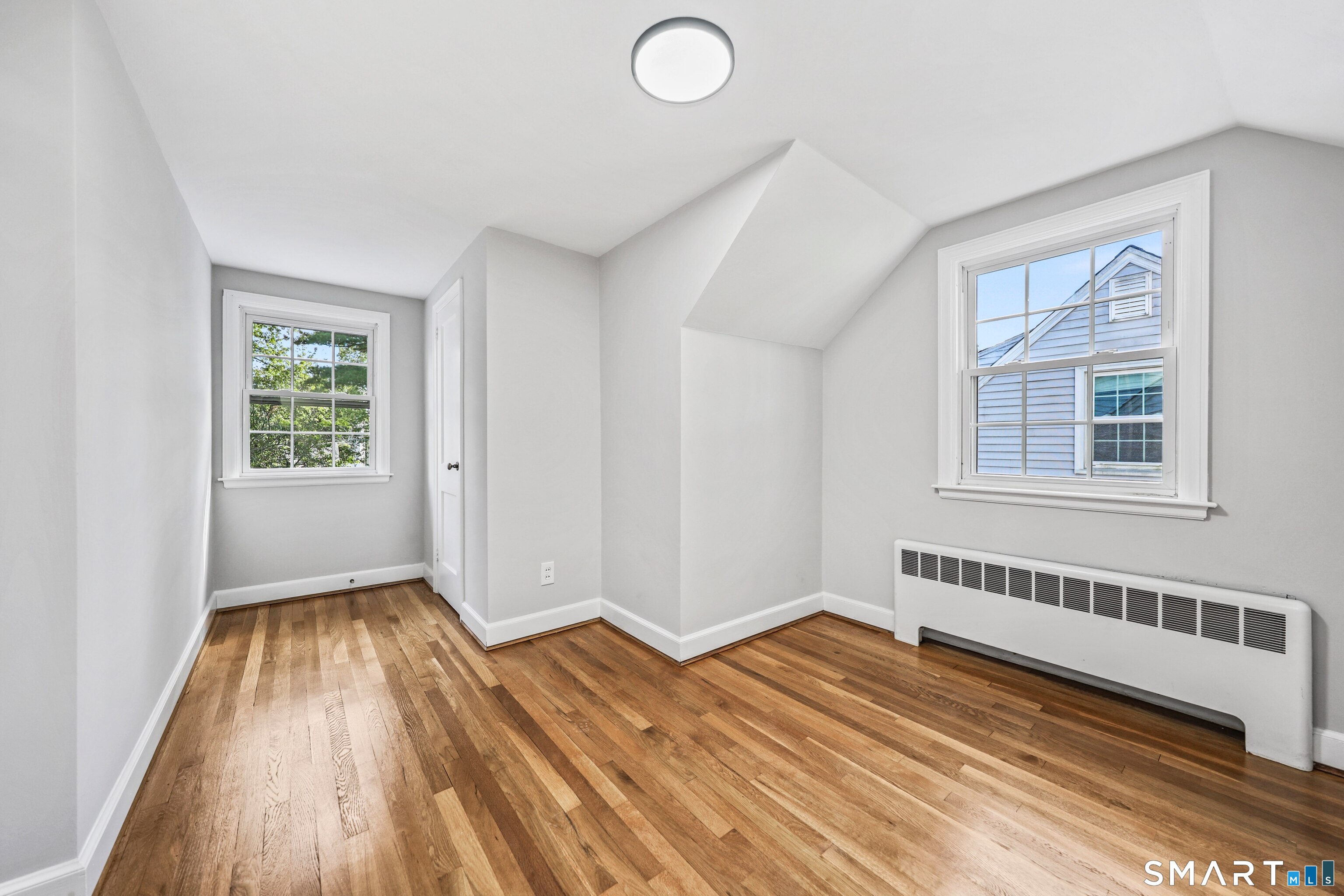 Empty room with hardwood floors, a sloped ceiling, and two windows.