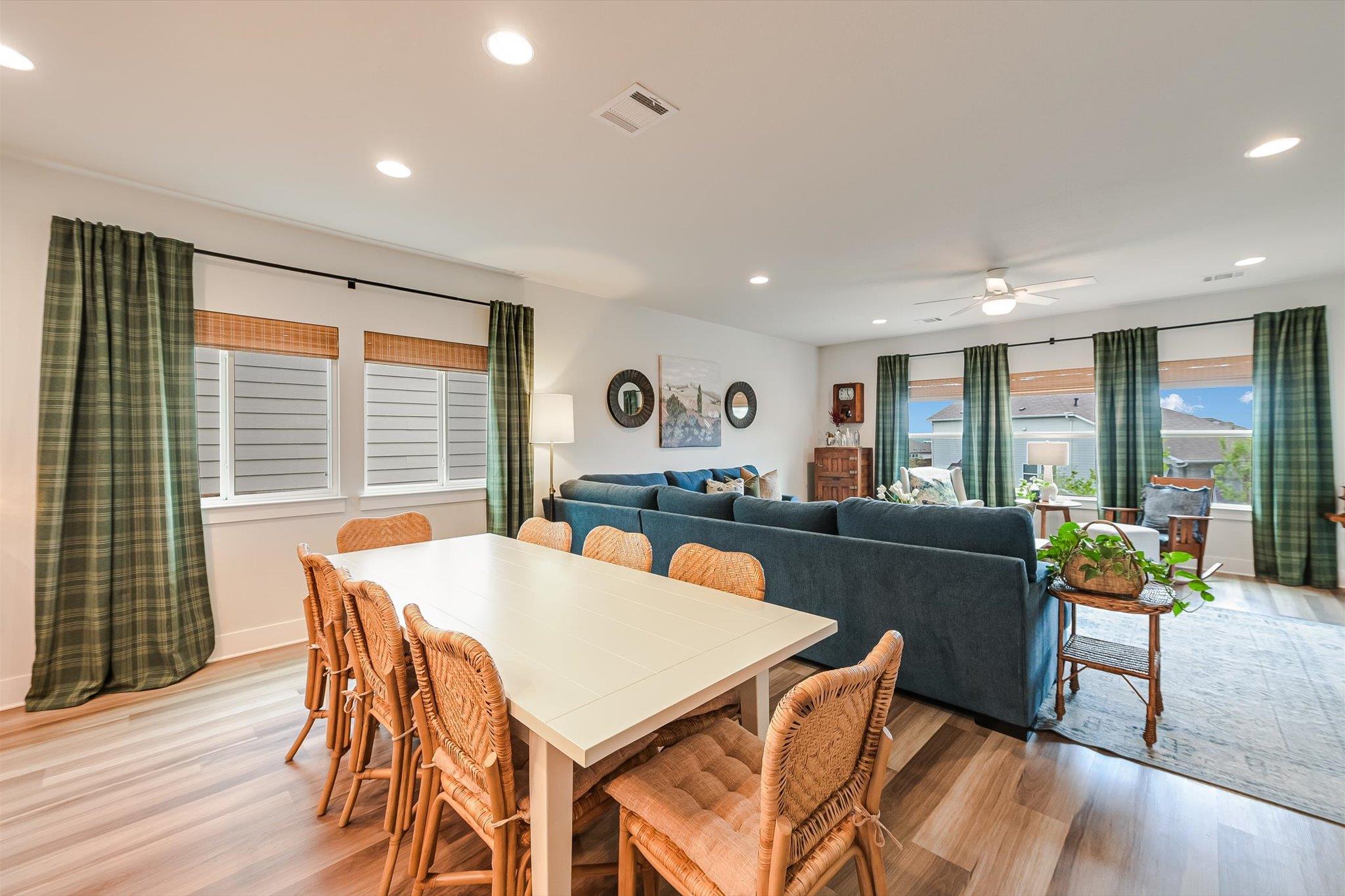 Open-plan dining and living room with woven chairs, a blue sectional, and green plaid curtains.