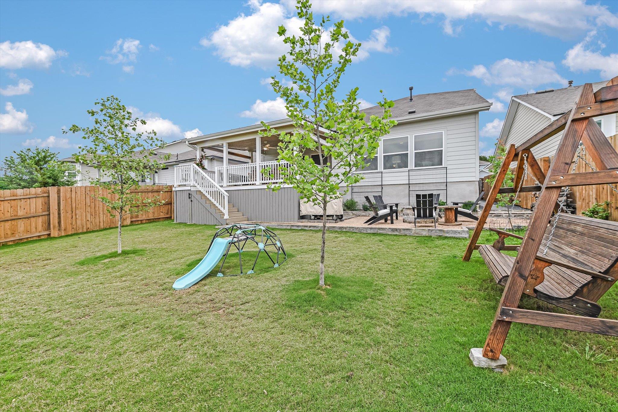 Fenced backyard with a raised deck, children's play equipment, lawn, and wooden porch swing.