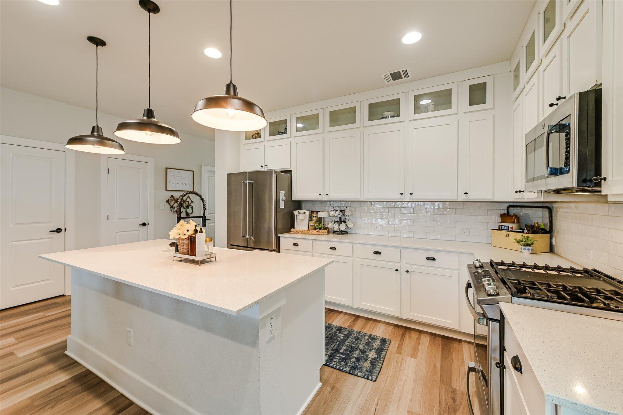 Bright white kitchen with a large island, stainless steel appliances, and three pendant lights.