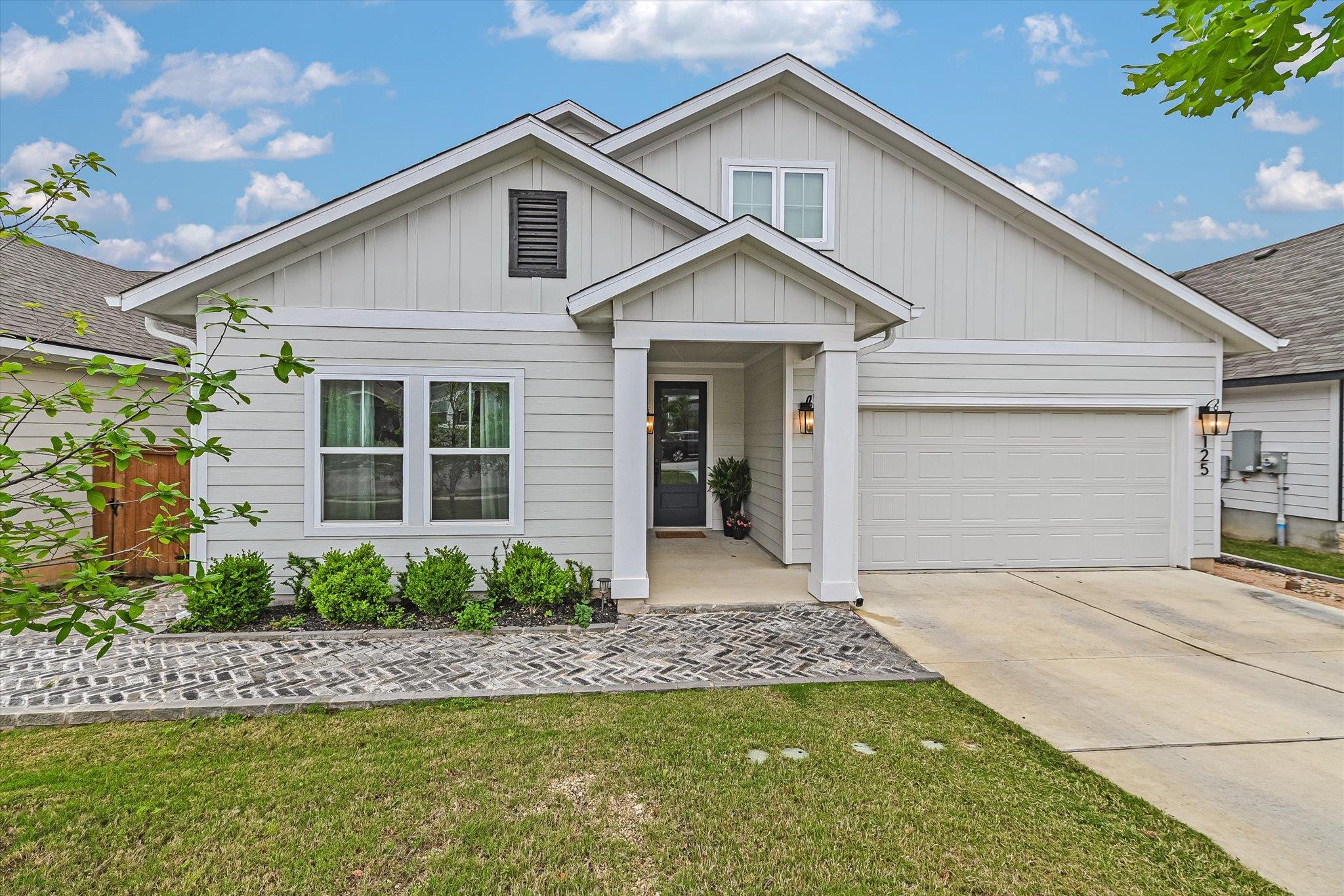 Light gray two-story house with a covered entry, double garage, and brick paver walkway.