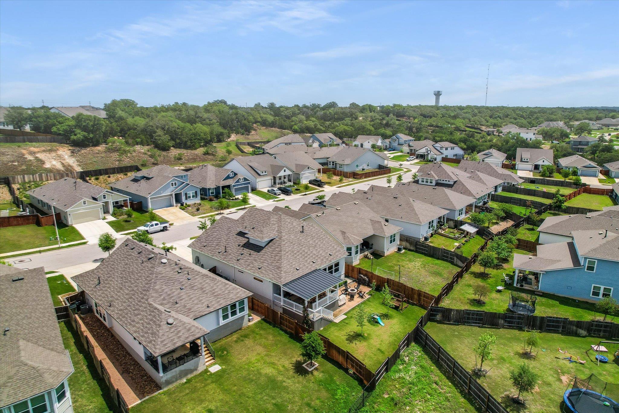 Aerial view of a residential home with a covered patio and fenced backyard among neighboring houses.