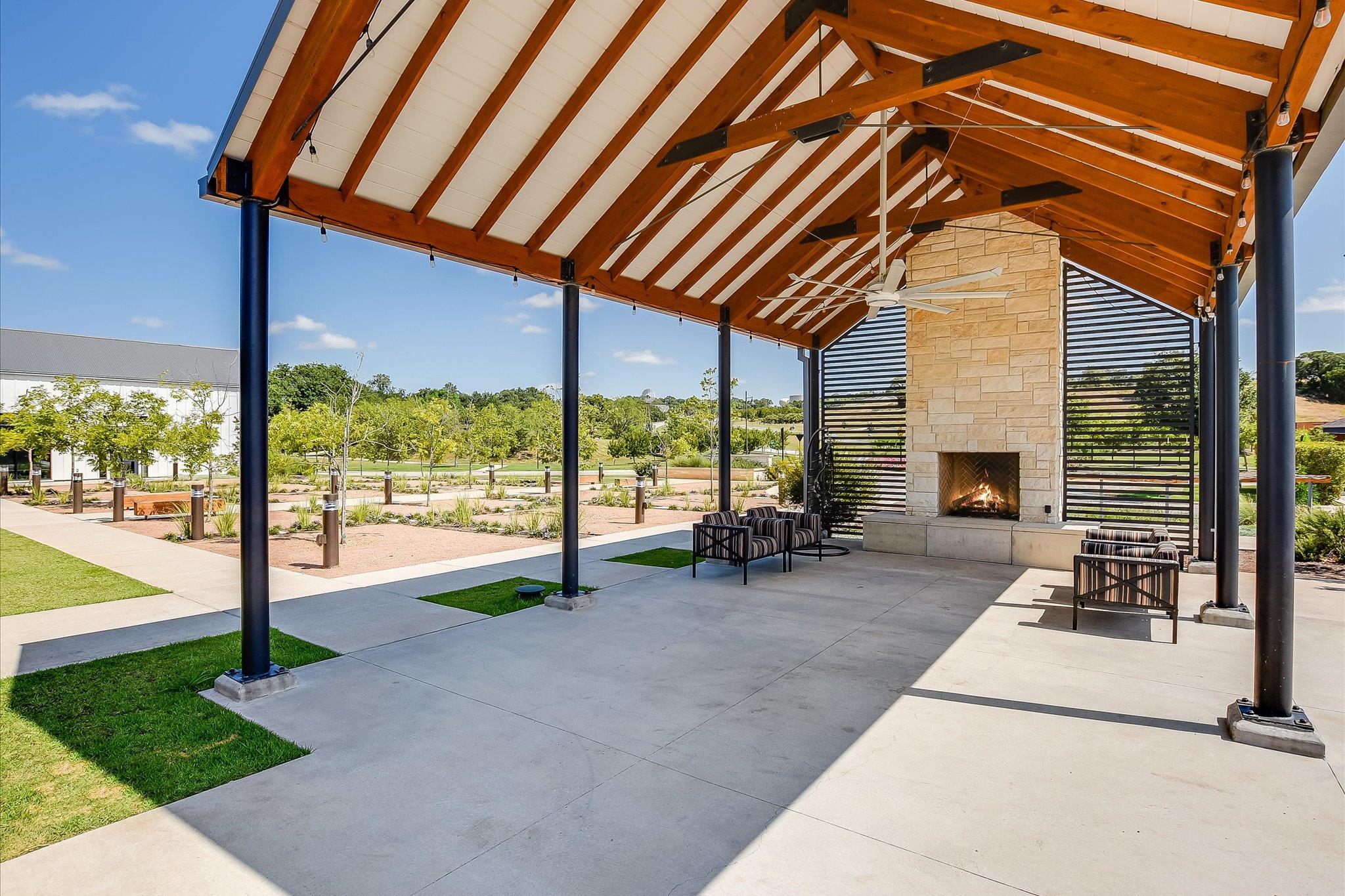 Covered patio with timber rafters, stone fireplace, and lounge seating.