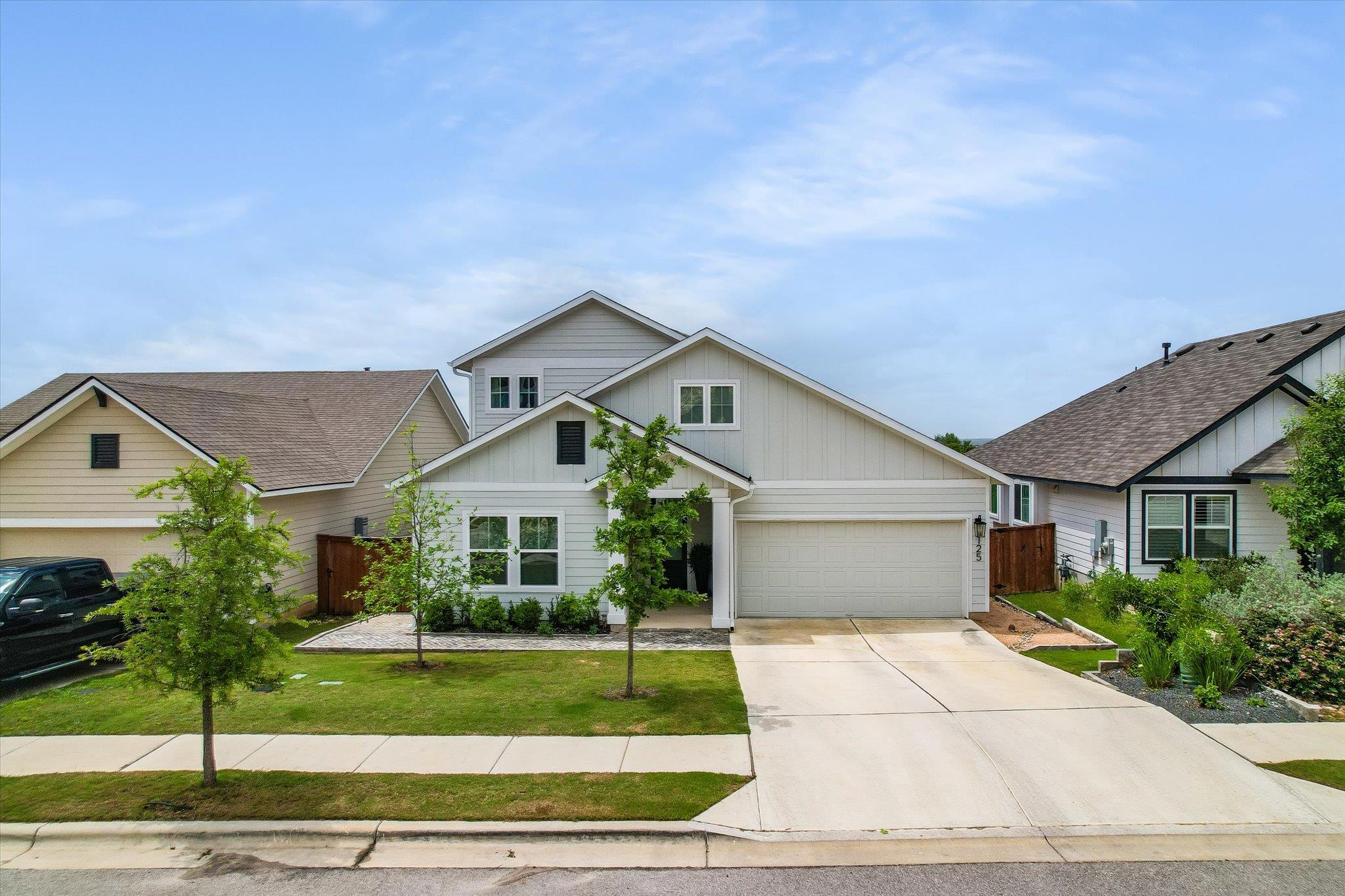 Two-story light-colored home with a double garage, broad driveway, and young trees in the front yard.