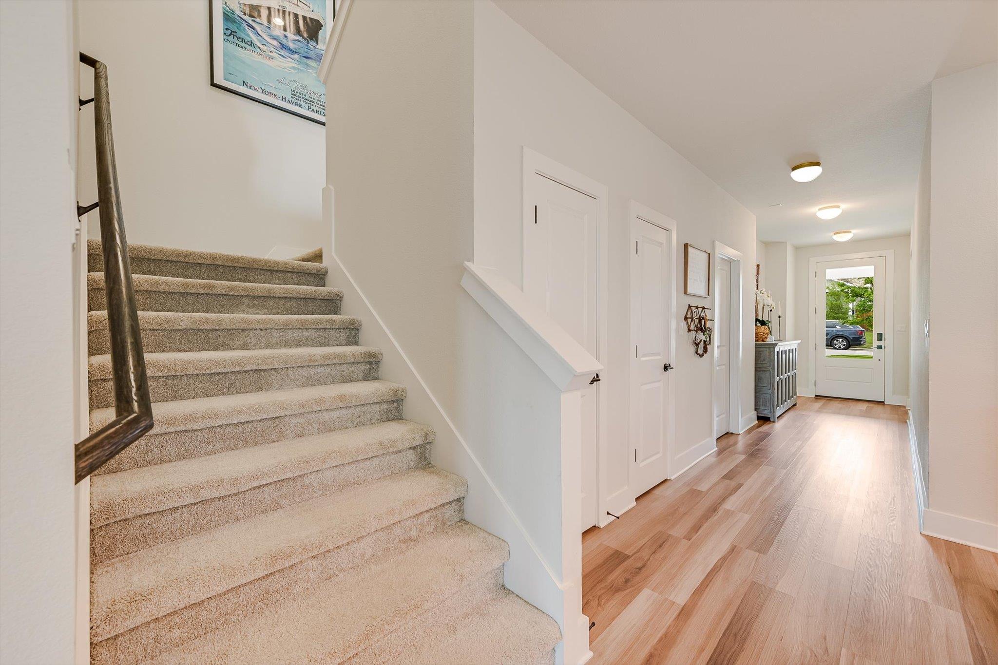 Entry hall with carpeted staircase beside a wood-floored hallway leading to the glass-paneled front door.