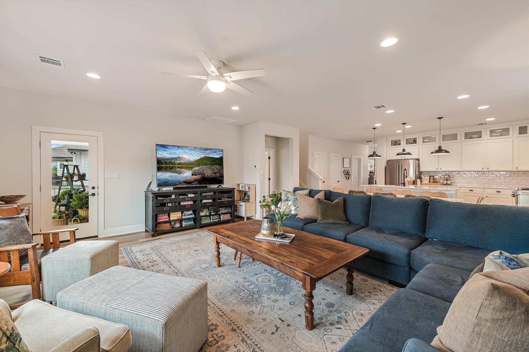 Open-plan living room with a blue sectional, wood coffee table, and adjoining white kitchen.