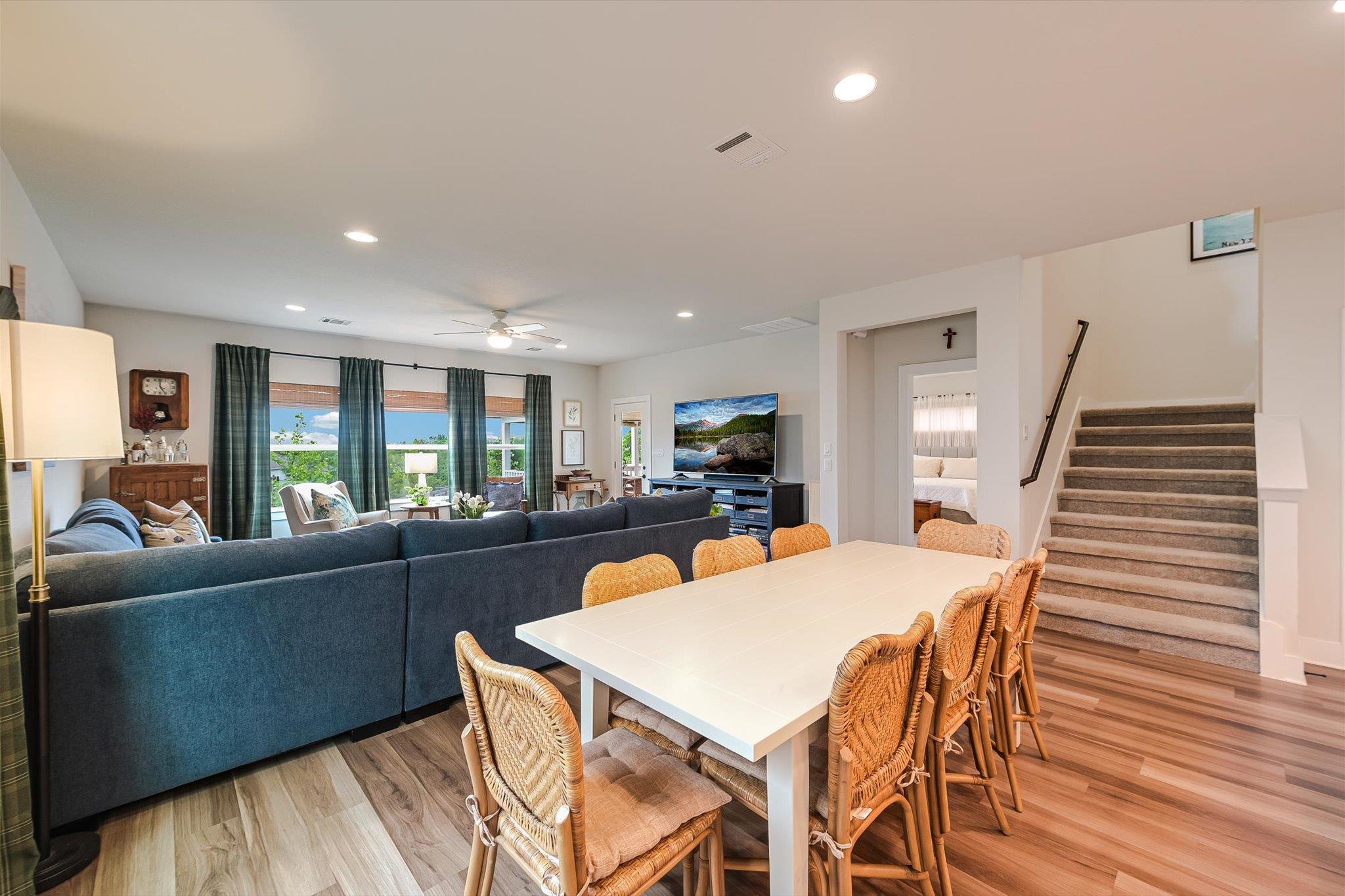 Open-plan living and dining area with a white table, wicker chairs, blue sectional, and carpeted stairs.