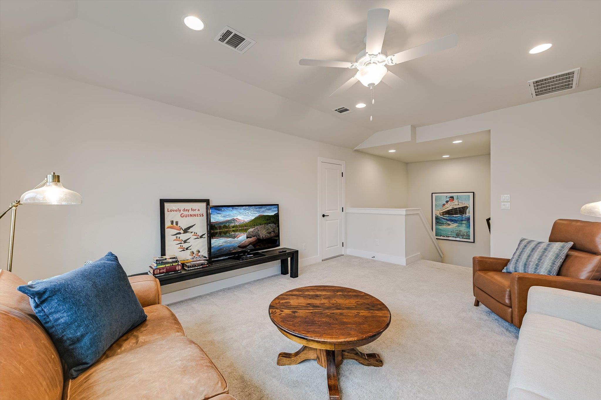 Furnished living room with tan leather seating, round wooden coffee table, ceiling fan, and stairway.