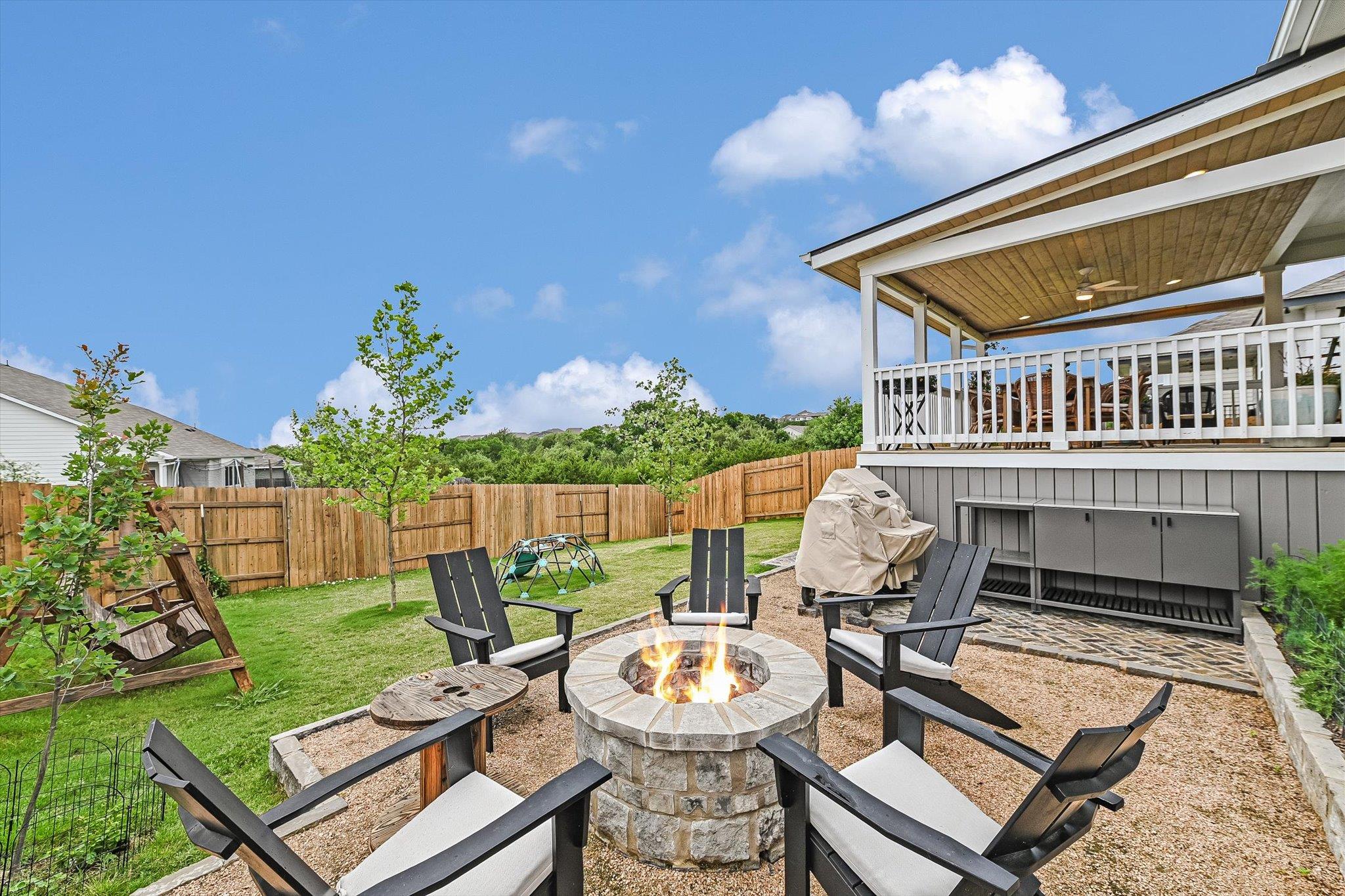 Backyard patio with a stone fire pit and Adirondack chairs beside a covered deck.