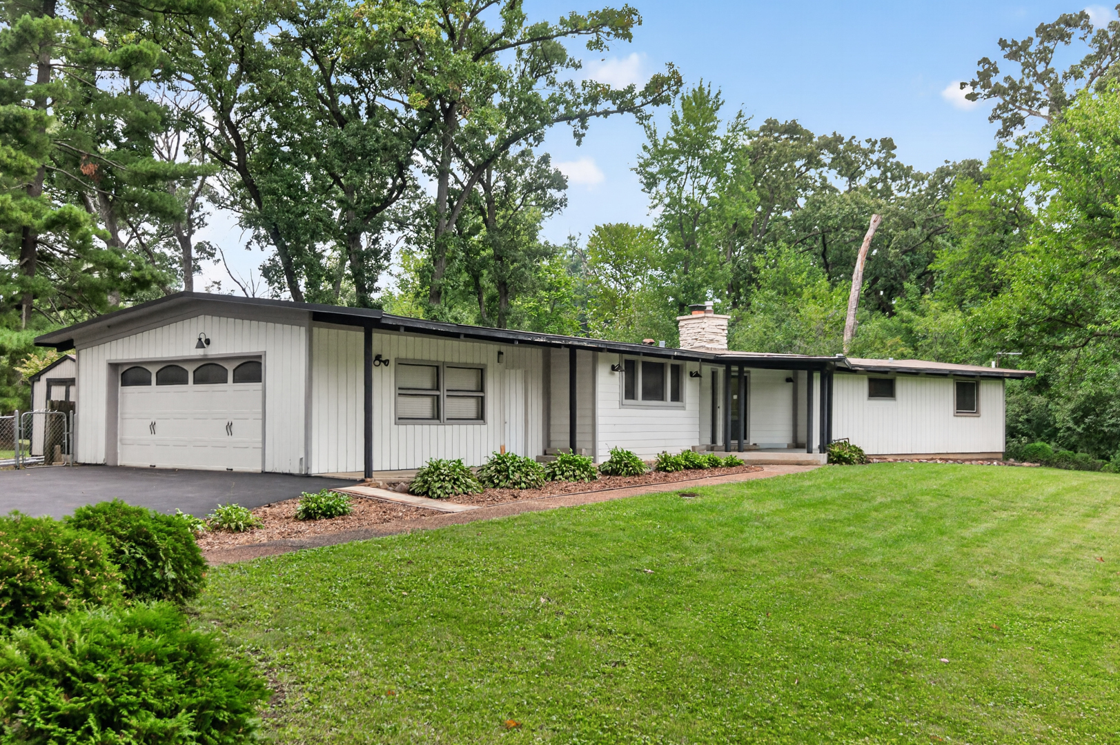 Single-story white house with attached garage, landscaped lawn, and mature trees.
