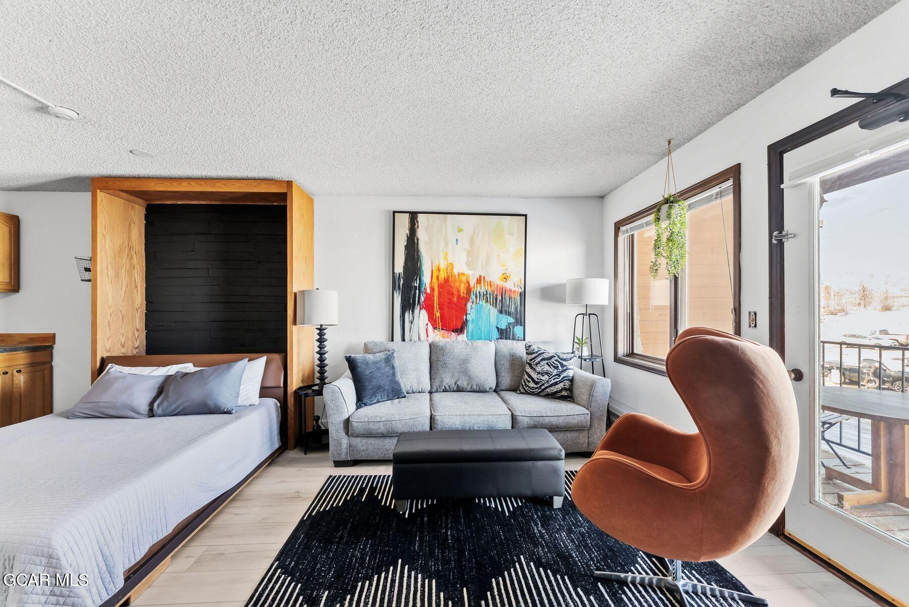 Furnished studio bedroom and living area with a wood-framed bed, gray sofa, and balcony door.