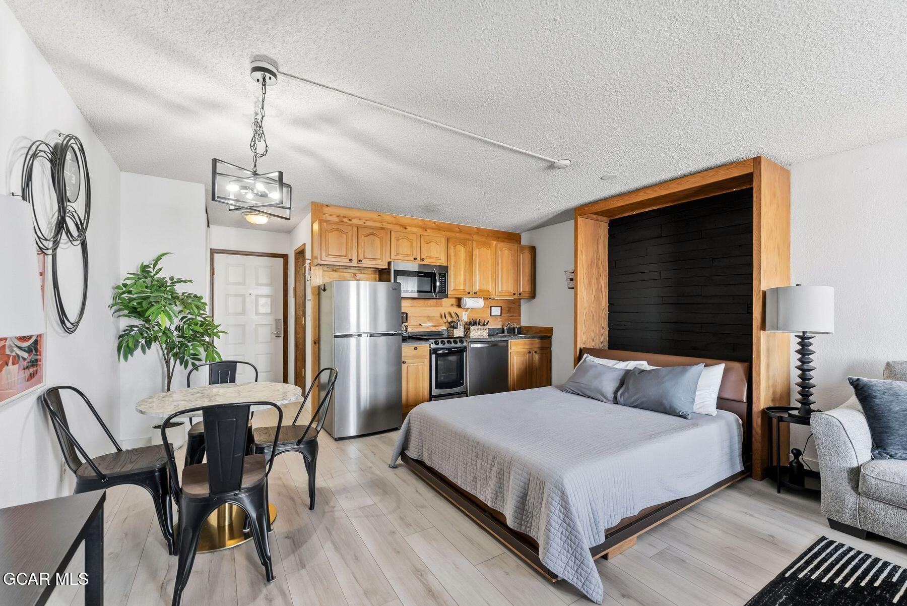 Furnished studio bedroom with a wood-framed bed beside a compact kitchen and dining area.