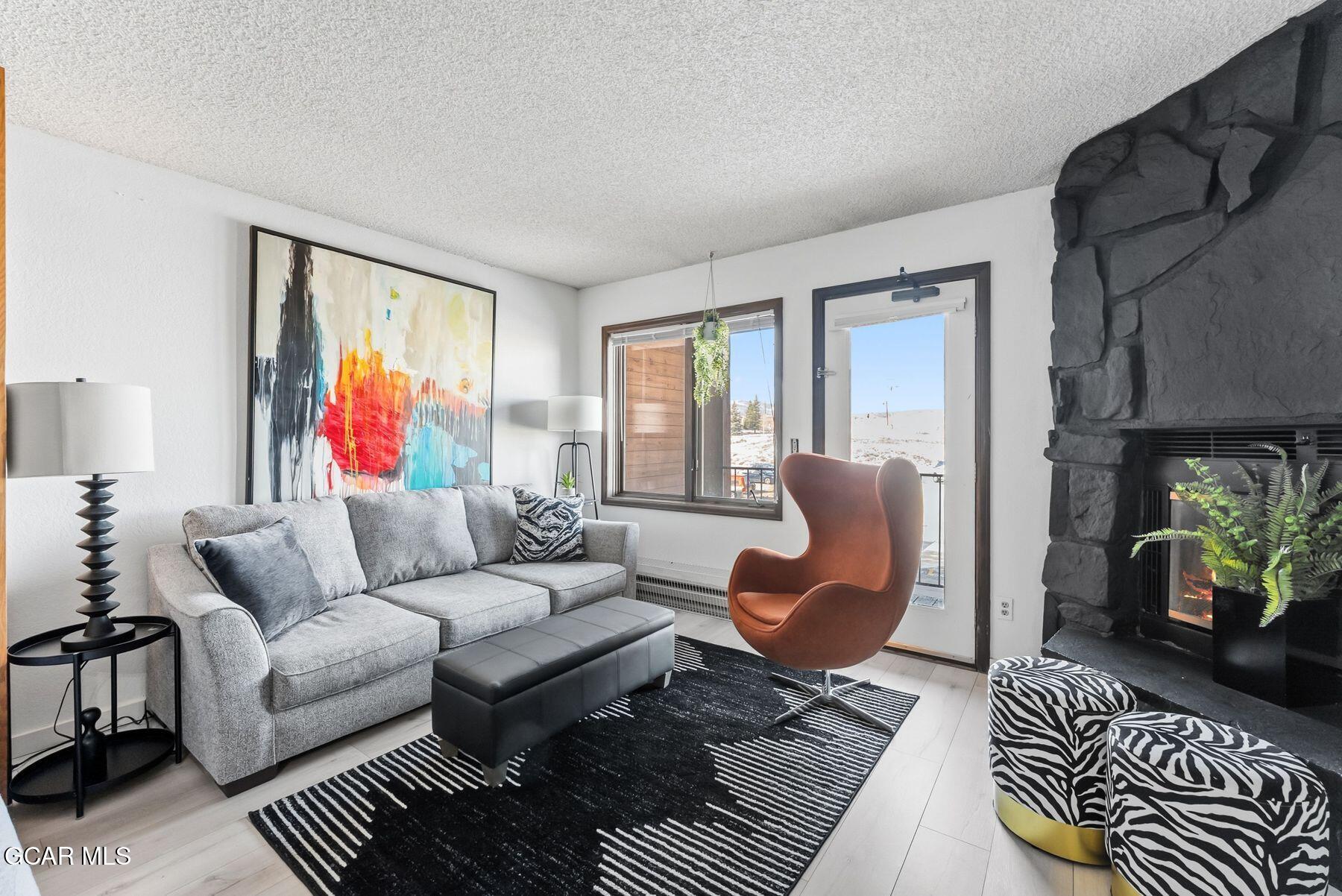 Living room with a gray sectional, rust-colored lounge chair, and dark stone fireplace.