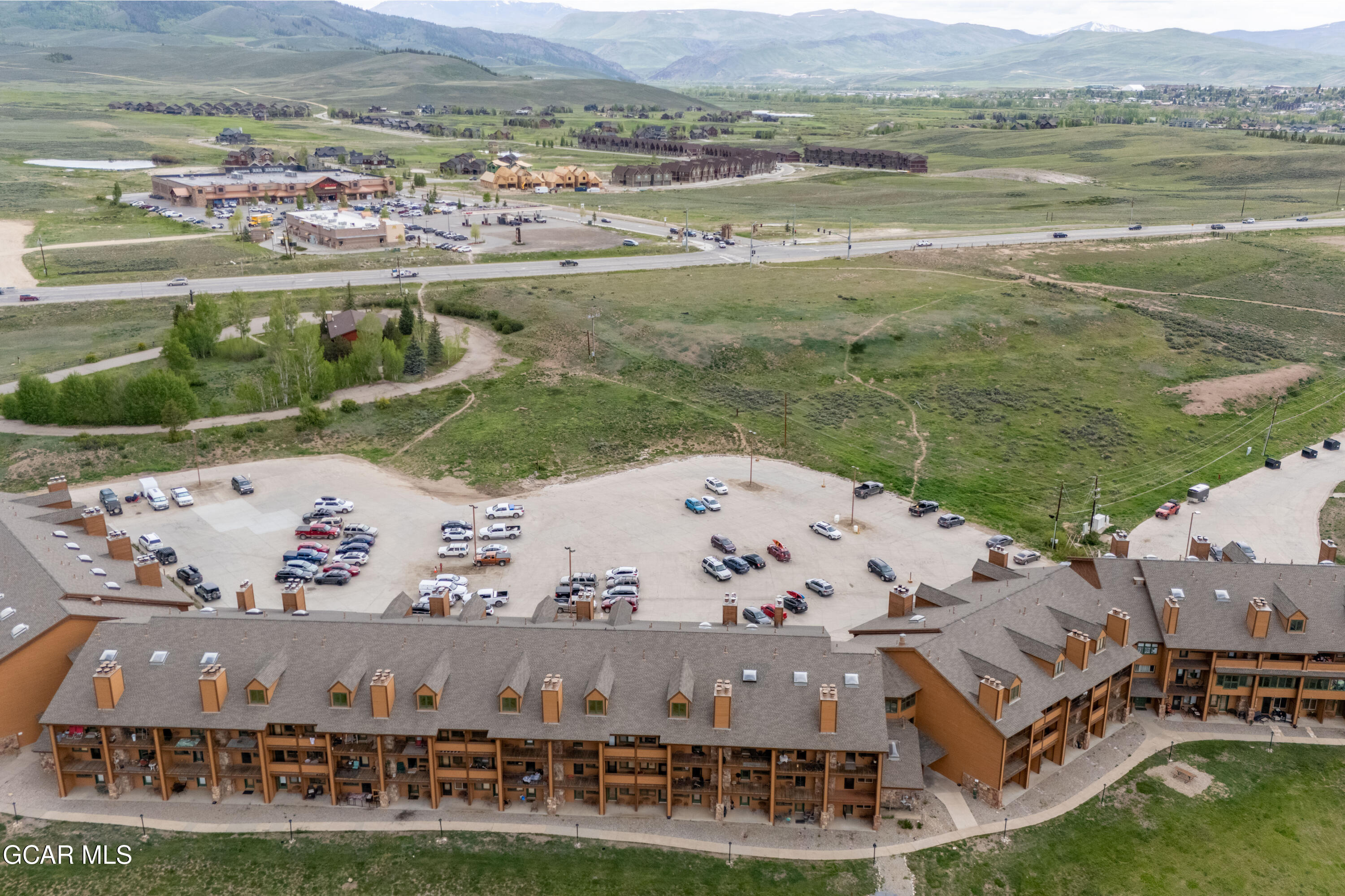 Aerial view of a mountain-area condominium complex with a large parking lot and highway nearby.