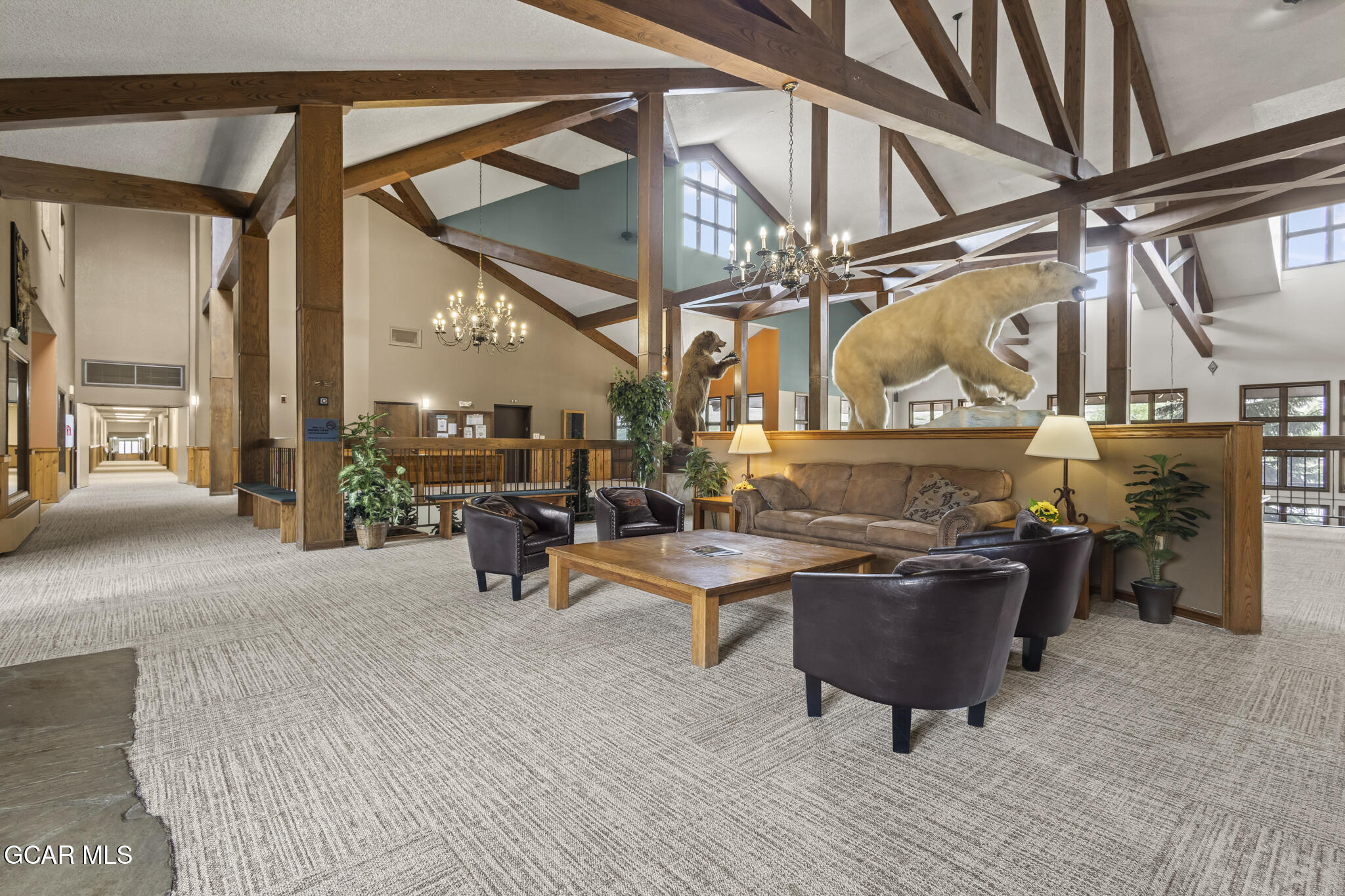 Furnished lodge lobby with exposed timber trusses, lounge seating, and mounted bear displays.