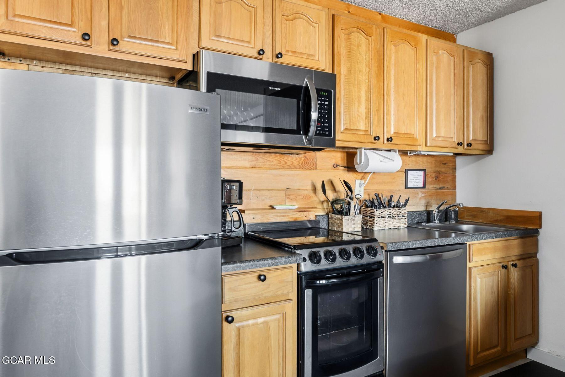 Kitchen with honey-colored wood cabinets, stainless steel appliances, and a plank backsplash.