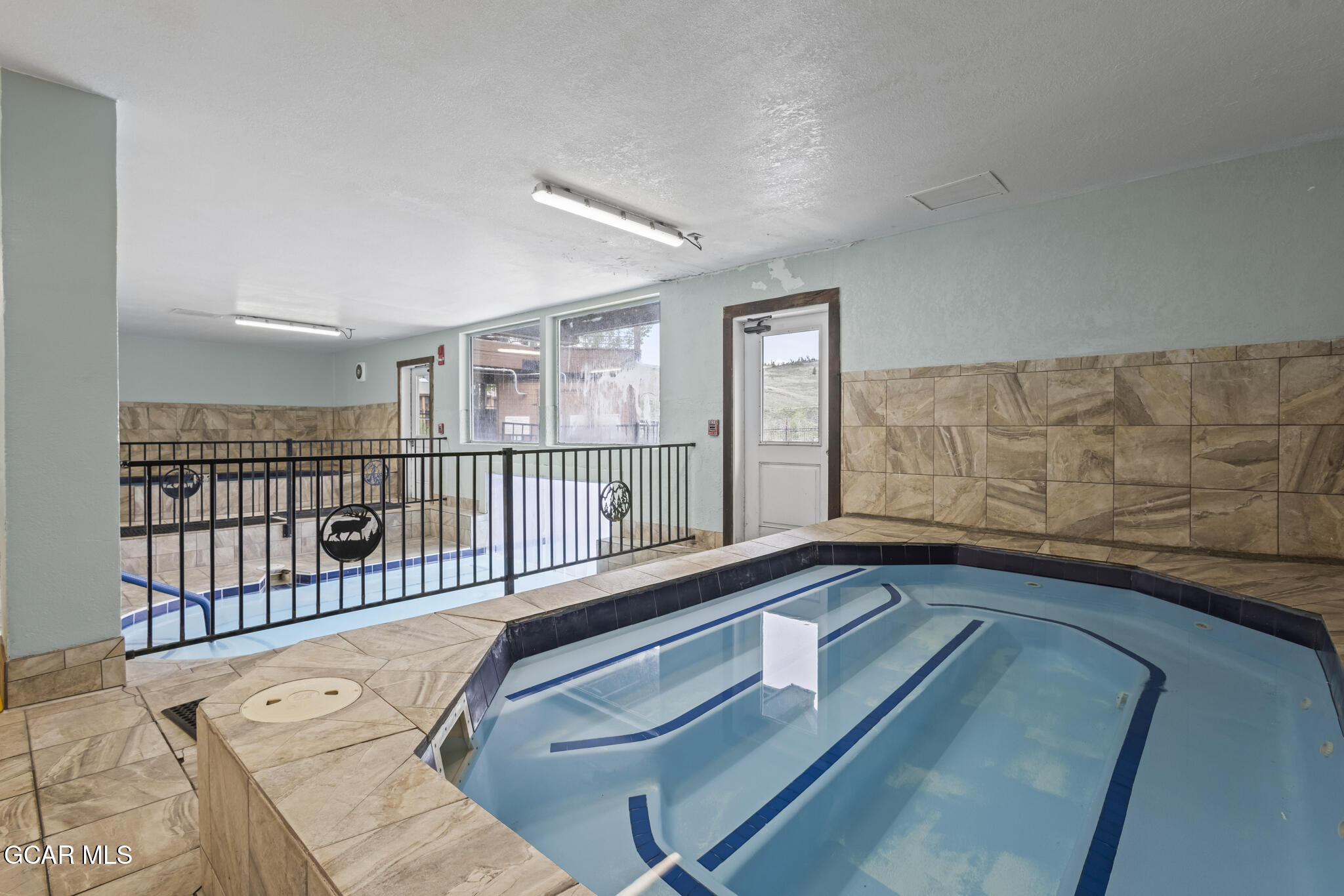 Indoor swimming pool with blue lane markings, tan tile surround, and black metal railing.