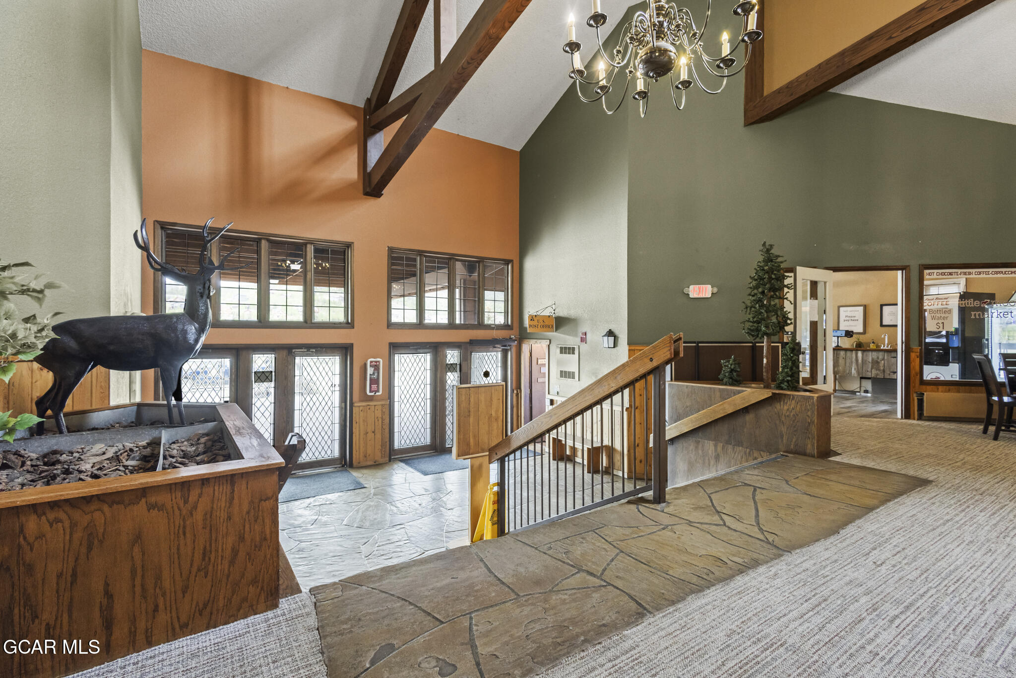 Lobby with vaulted timber beams, a chandelier, stone floors, and a prominent deer sculpture.