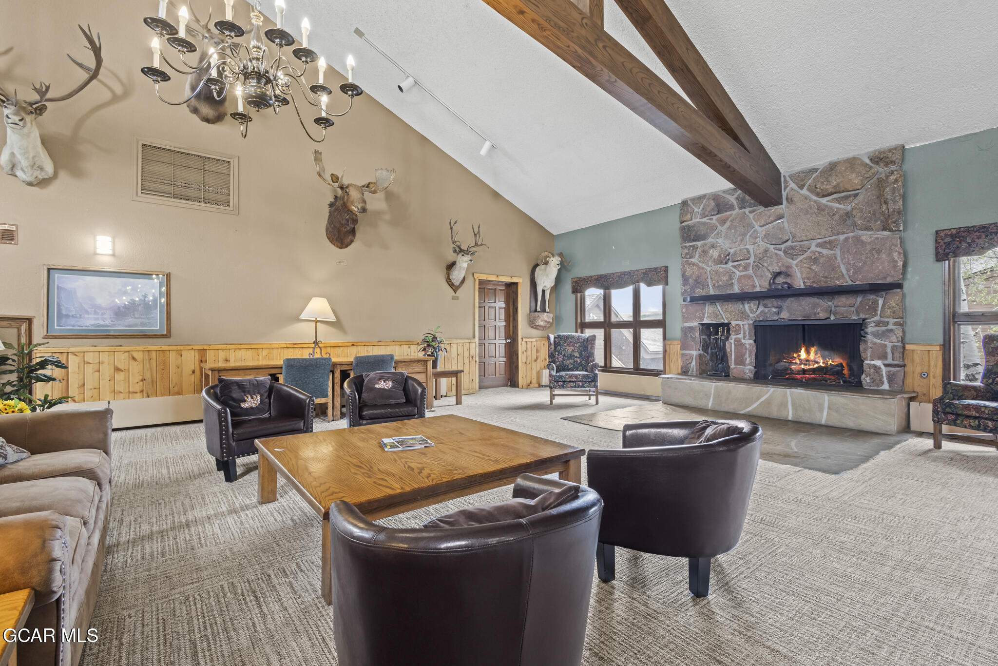 Lodge-style living room with a vaulted ceiling, stone fireplace, exposed beams, and leather chairs.