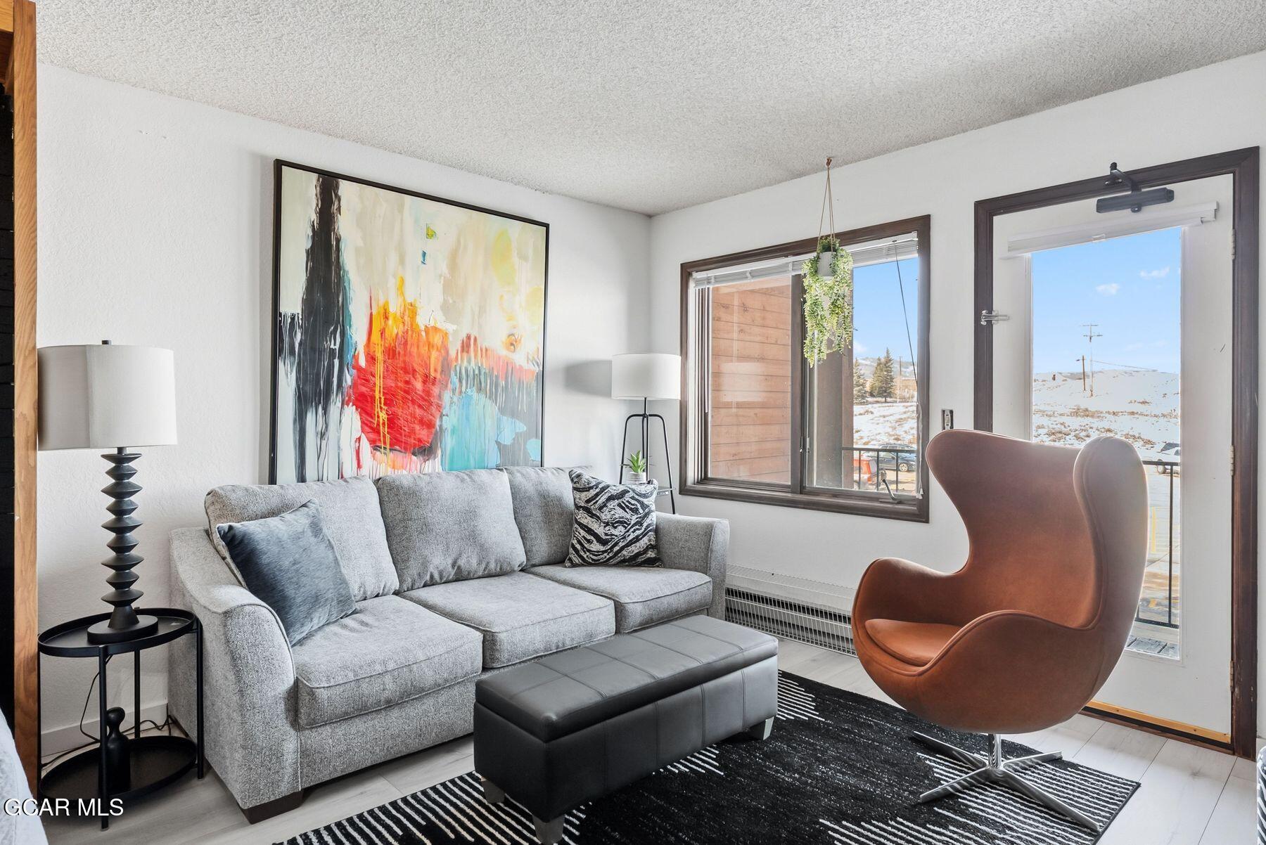 Living room with a gray sectional, sculptural brown chair, and sliding glass door overlooking snowy hills.