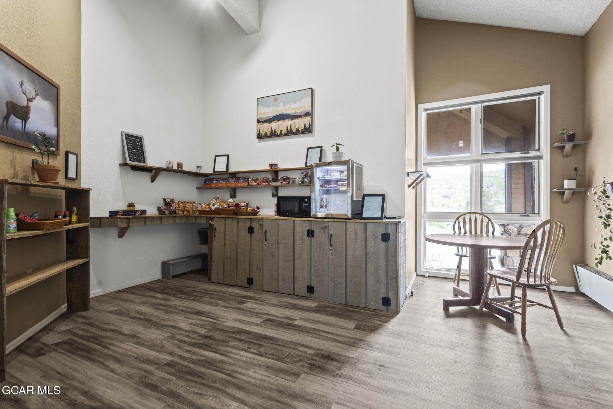 Interior snack shop with stocked shelves, a wood counter, refrigerator, and window-side seating.