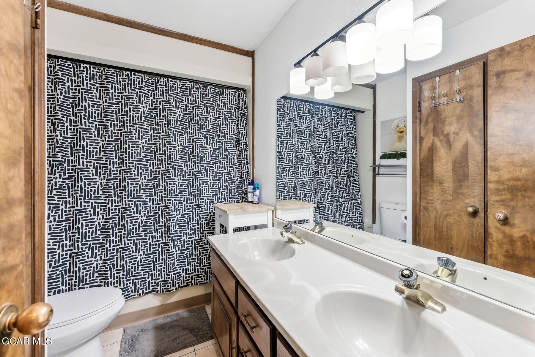 Bathroom with a double vanity, patterned shower curtain, large mirror, and wood cabinetry.