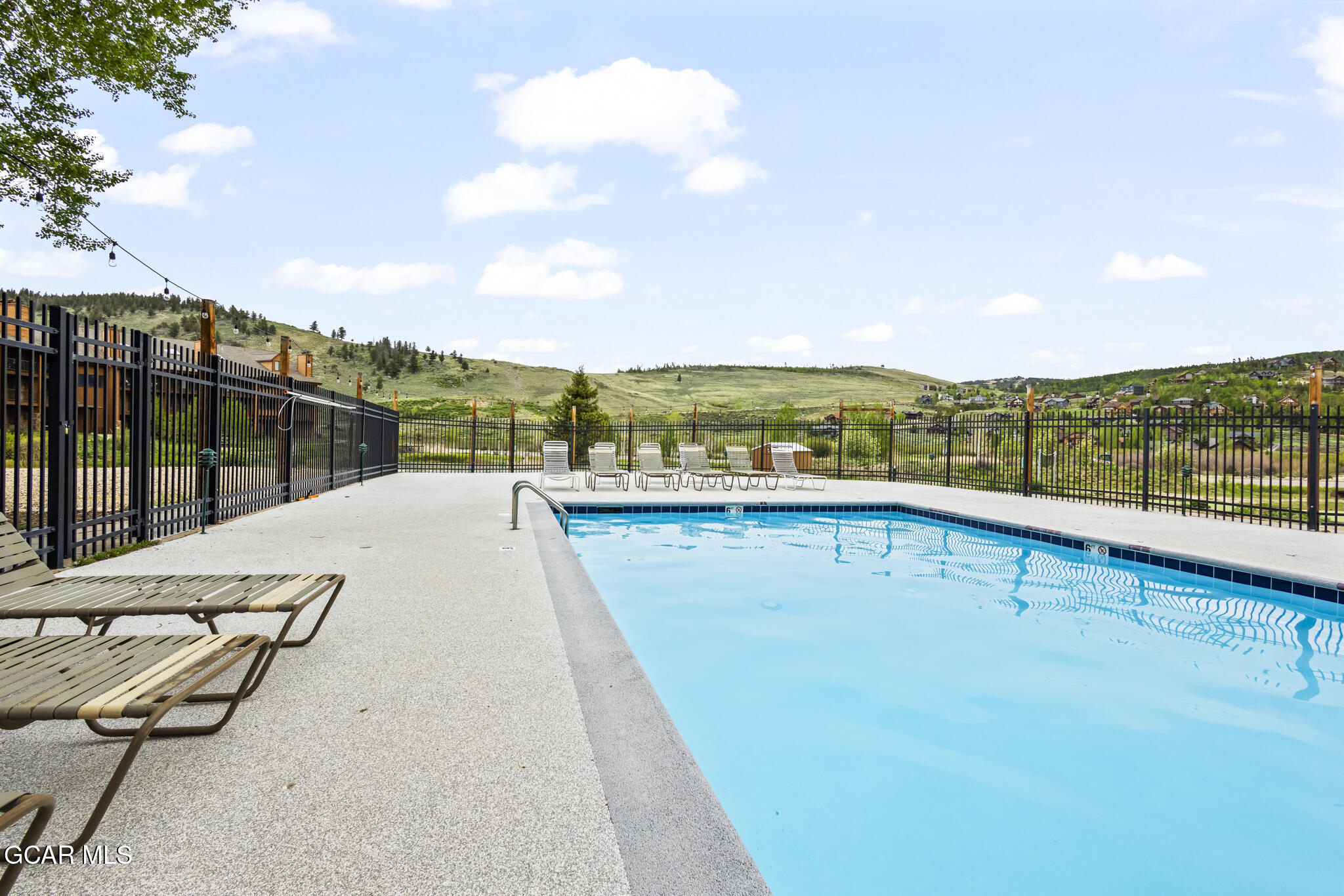 Outdoor pool with lounge chairs, black fencing, and rolling green hills beyond.