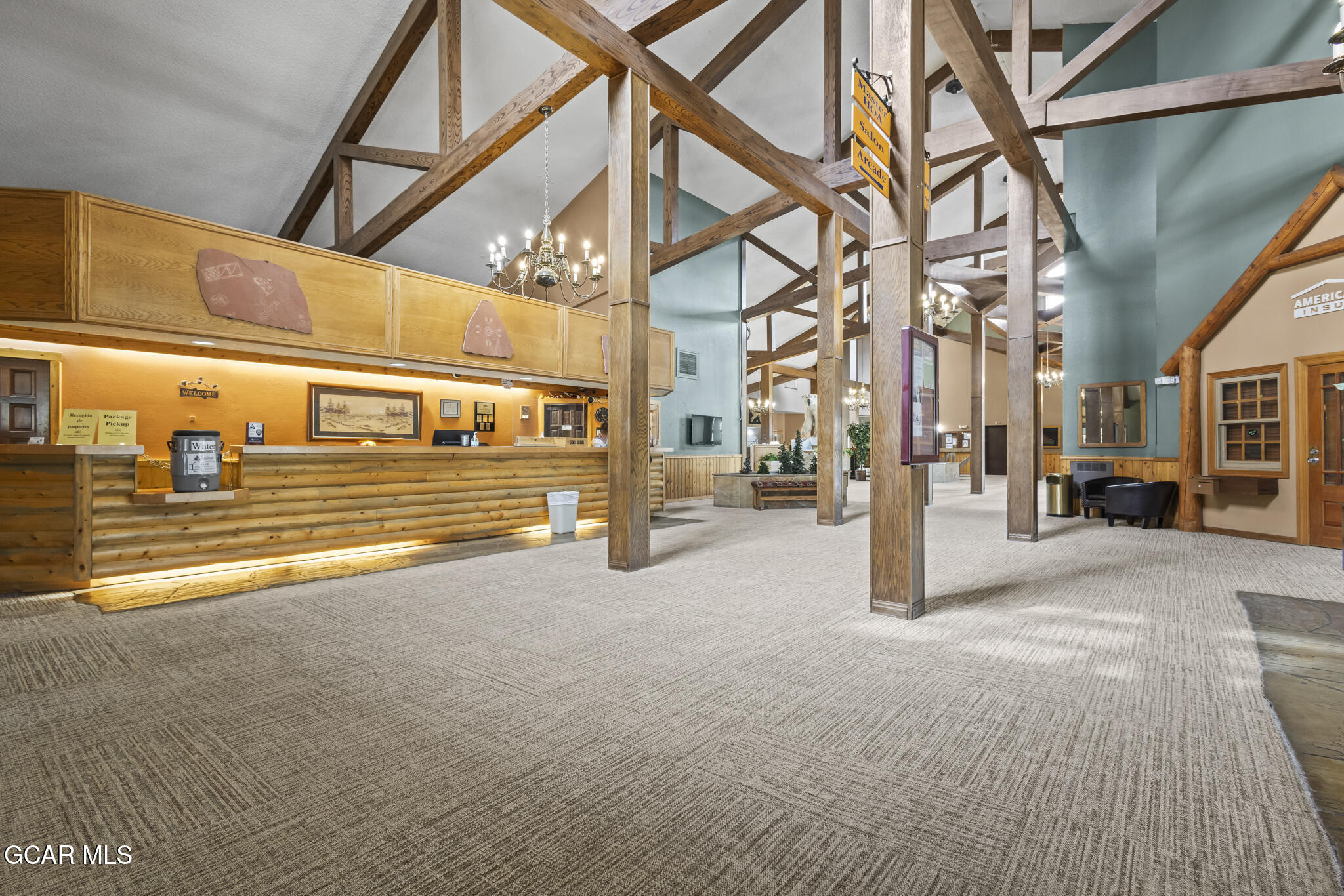 Commercial lobby with a log-style reception desk, soaring timber beams, and chandeliers.
