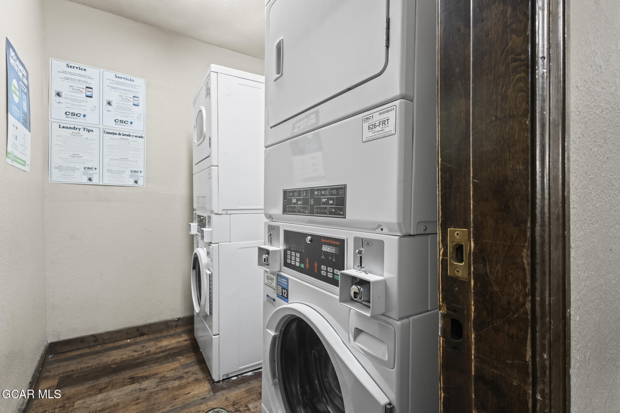 Laundry room with commercial washers and dryers, instruction posters, and dark wood-look flooring.