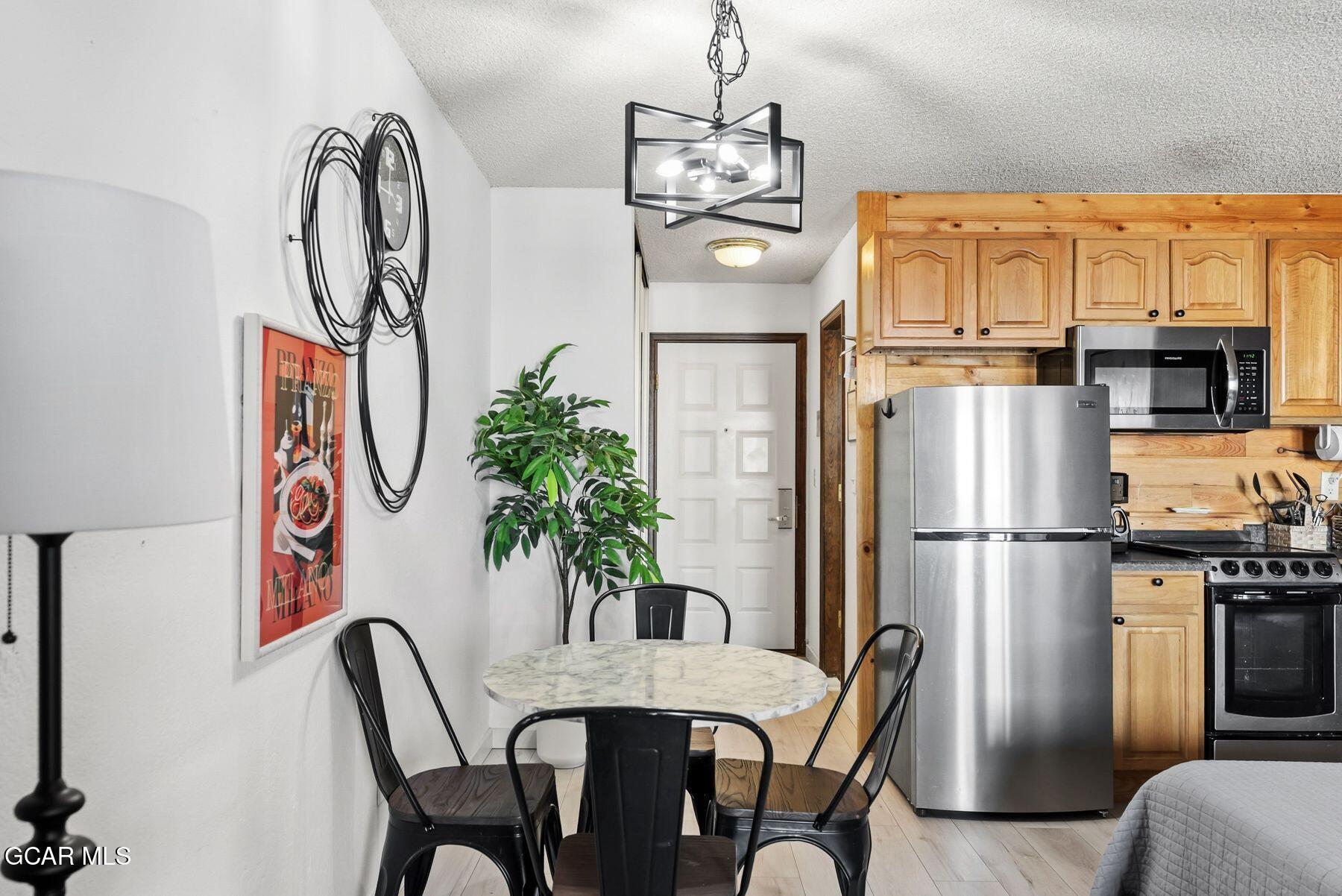 Kitchen and dining area with wood cabinets, stainless steel appliances, and a round table with black chairs.