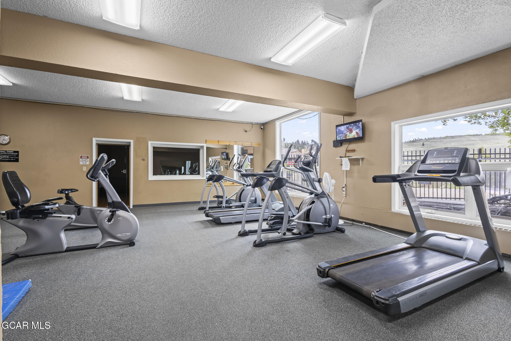 Community fitness room with treadmills, ellipticals, stationary bikes, and large windows.