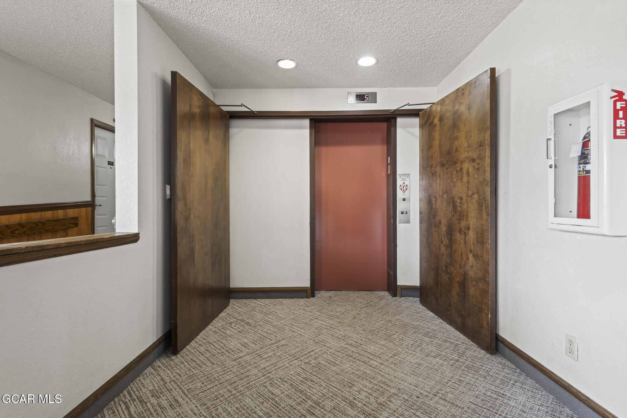 Elevator lobby with open wooden doors, a red elevator, and patterned carpet.