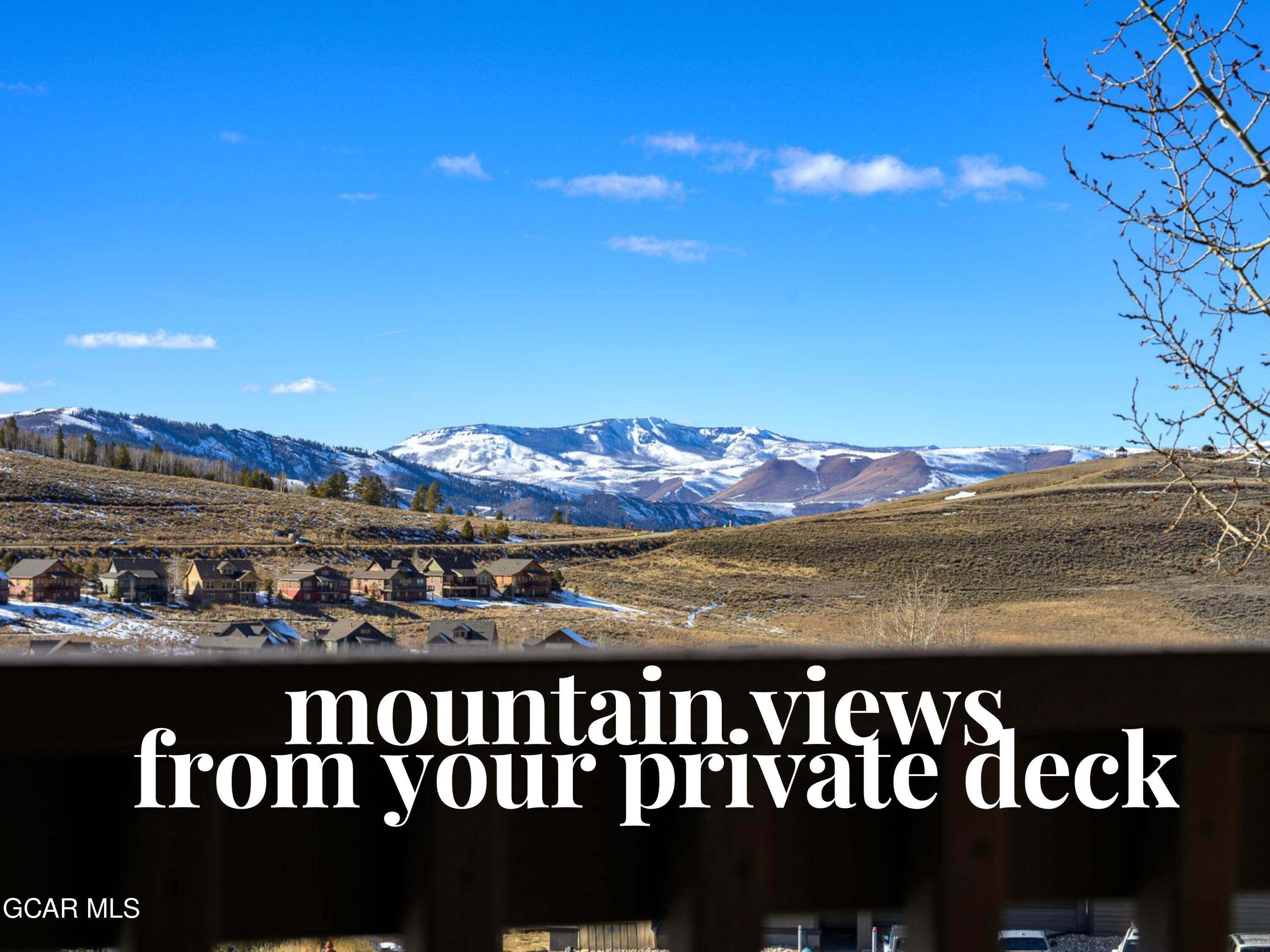 Snow-covered mountain range beyond a residential community, viewed from a private deck.