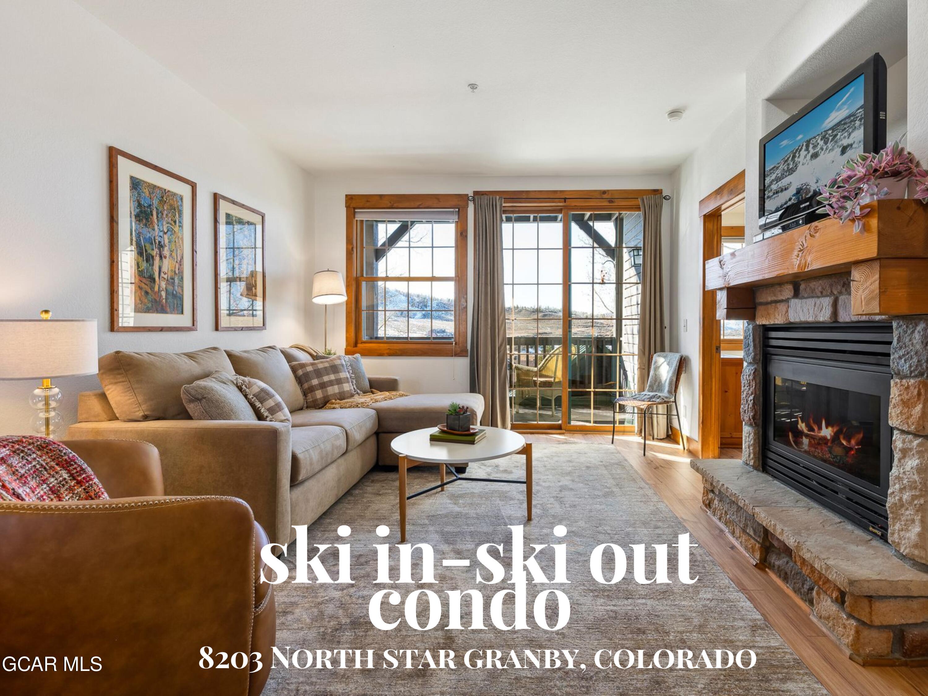 Condo living room with a stone fireplace, beige sectional, and balcony doors overlooking mountain scenery.