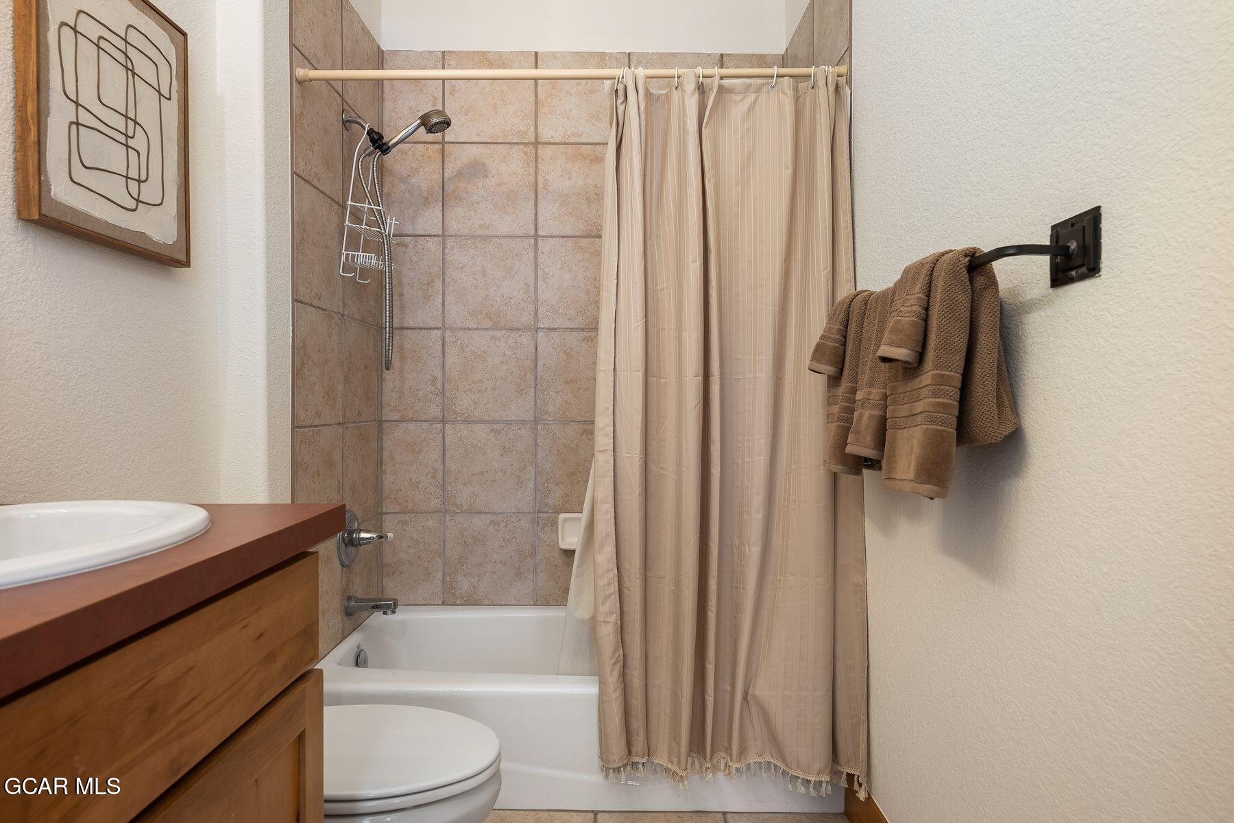 Bathroom with tiled tub and shower, beige curtain, wooden vanity, and brown towels.