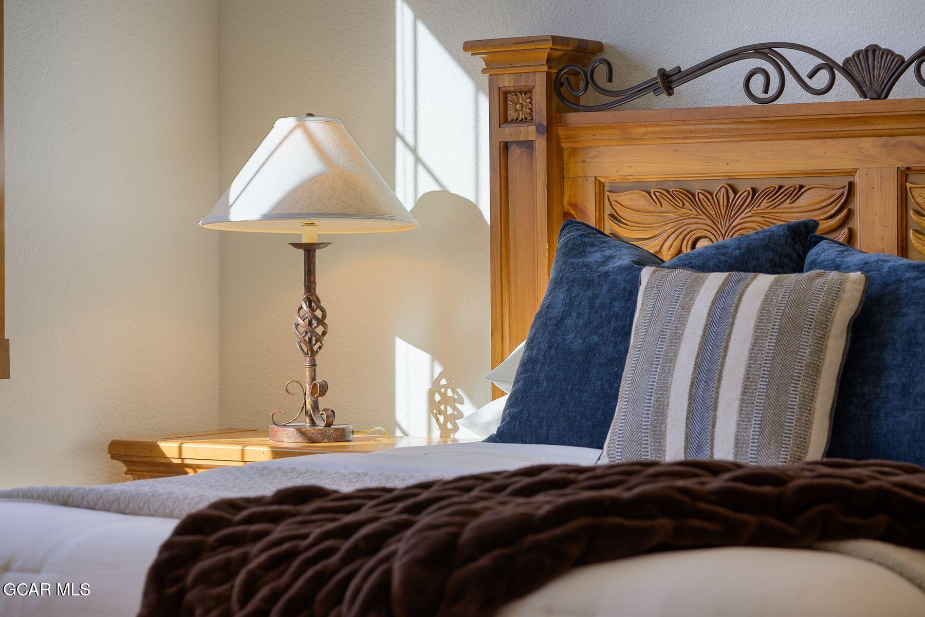 Bedroom with carved wooden headboard, navy pillows, patterned accent pillow, and bedside lamp.