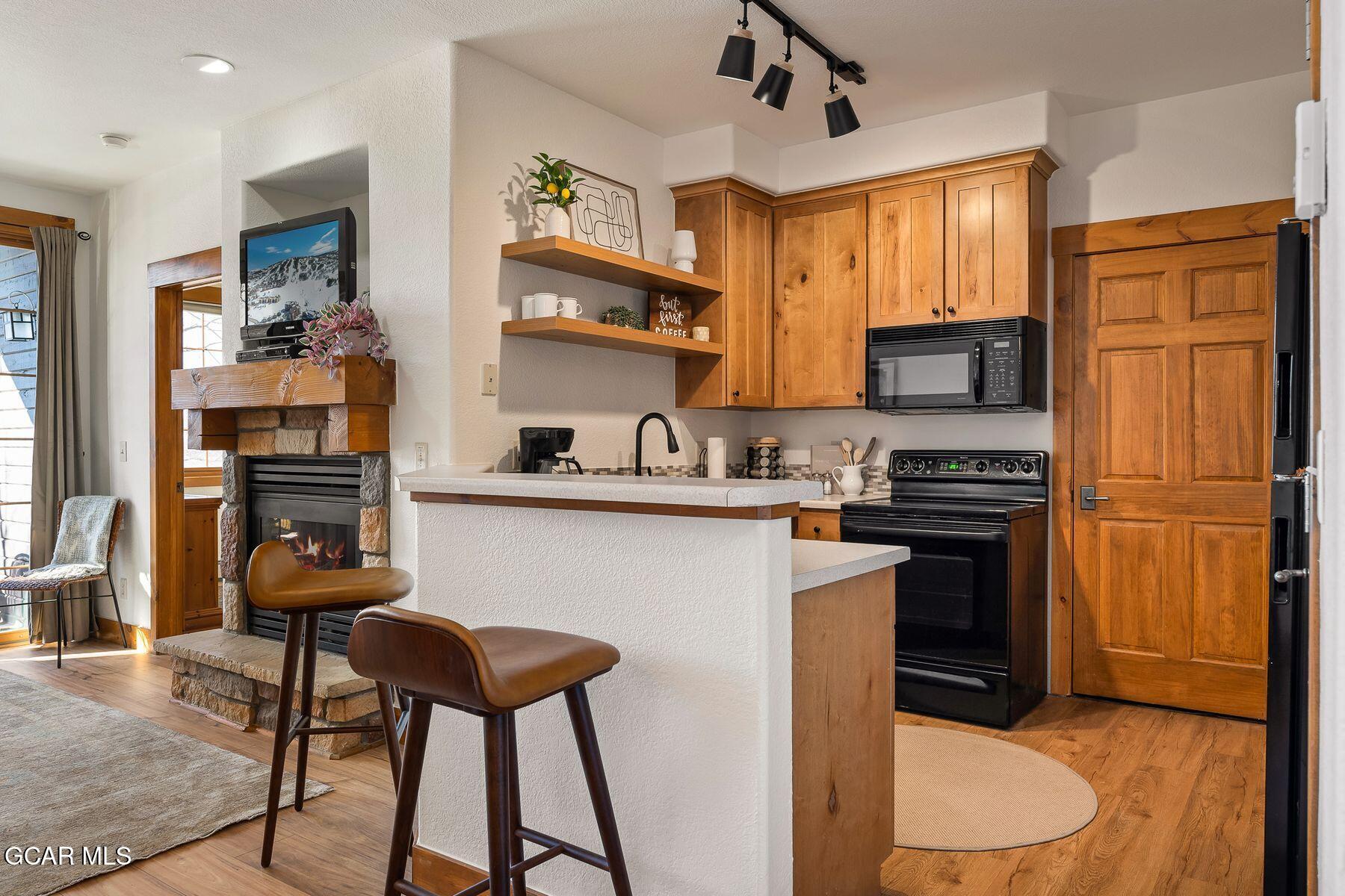 Kitchen and living area with wood cabinets, a breakfast counter, and a stone fireplace.