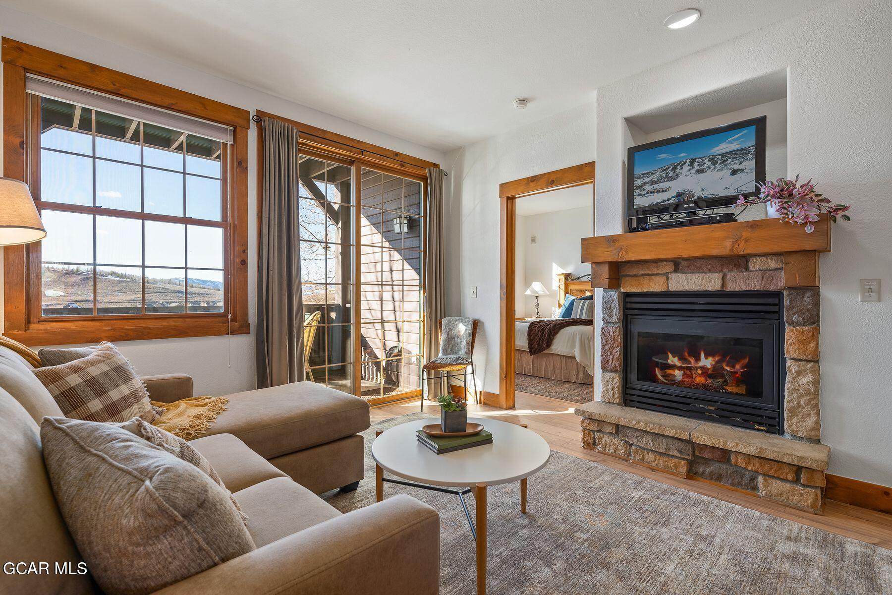 Living room with a stone fireplace, beige sectional, and windows overlooking the mountains.