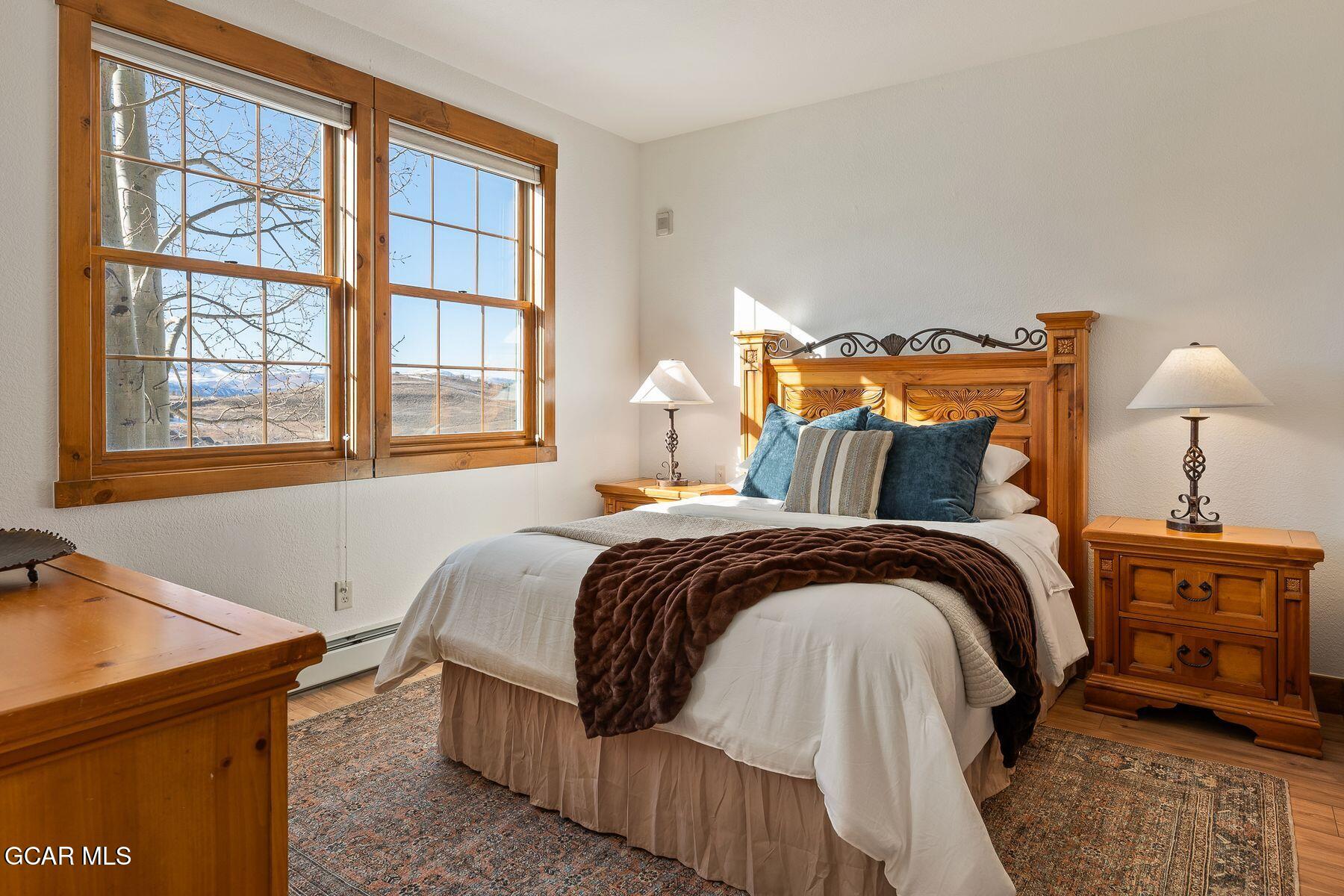 Furnished bedroom with a carved wooden bed and large windows overlooking distant mountains.