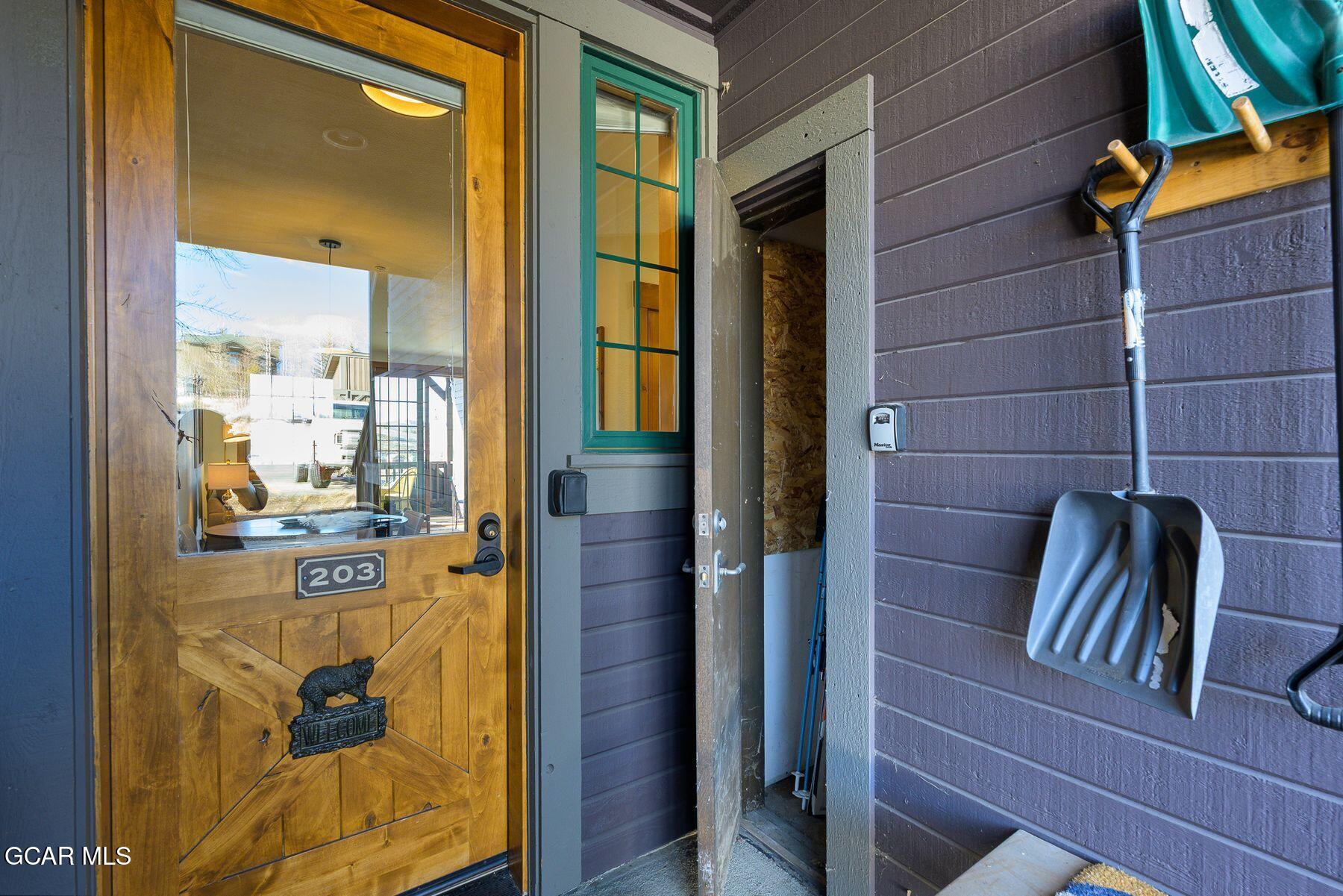 Unit 203 entrance with a wooden glass-paneled door and snow shovels on the siding.