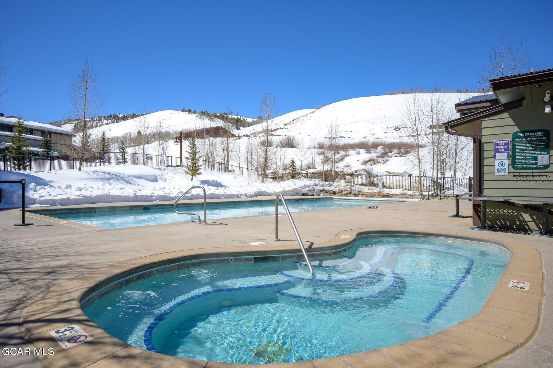 Outdoor pool and hot tub beside snow-covered hills at Granby Ranch.