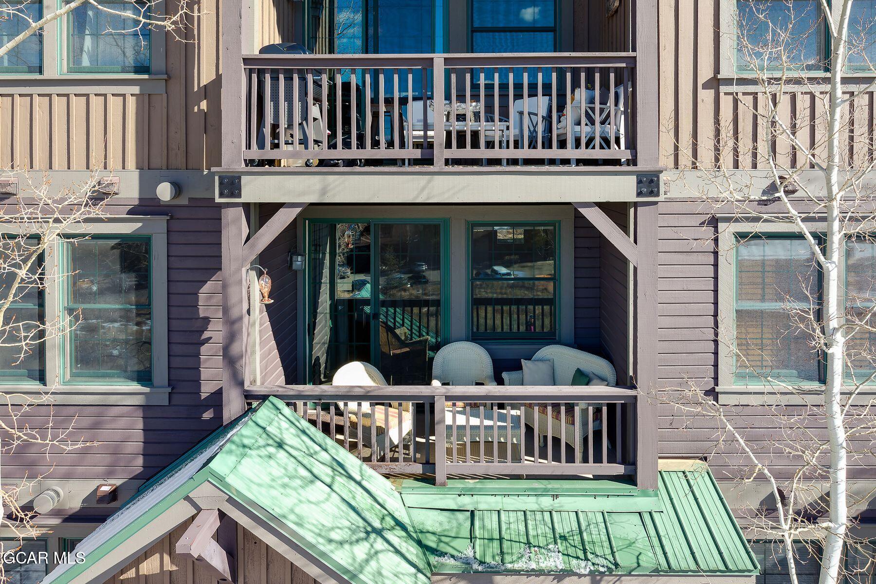 Condominium facade with stacked balconies, outdoor seating, and green metal roofing.
