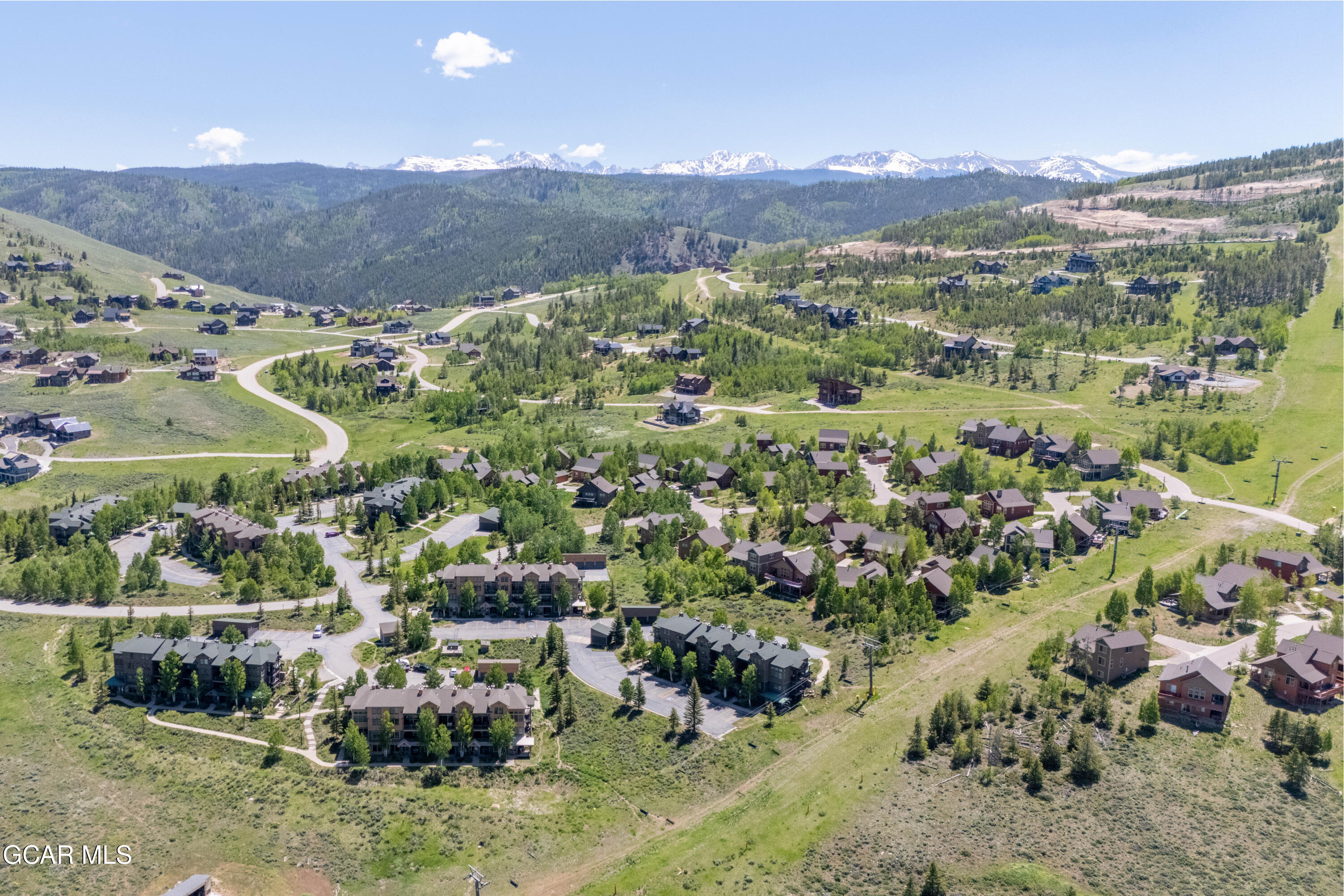 Aerial view of a mountain neighborhood with homes, winding roads, and snow-capped peaks.