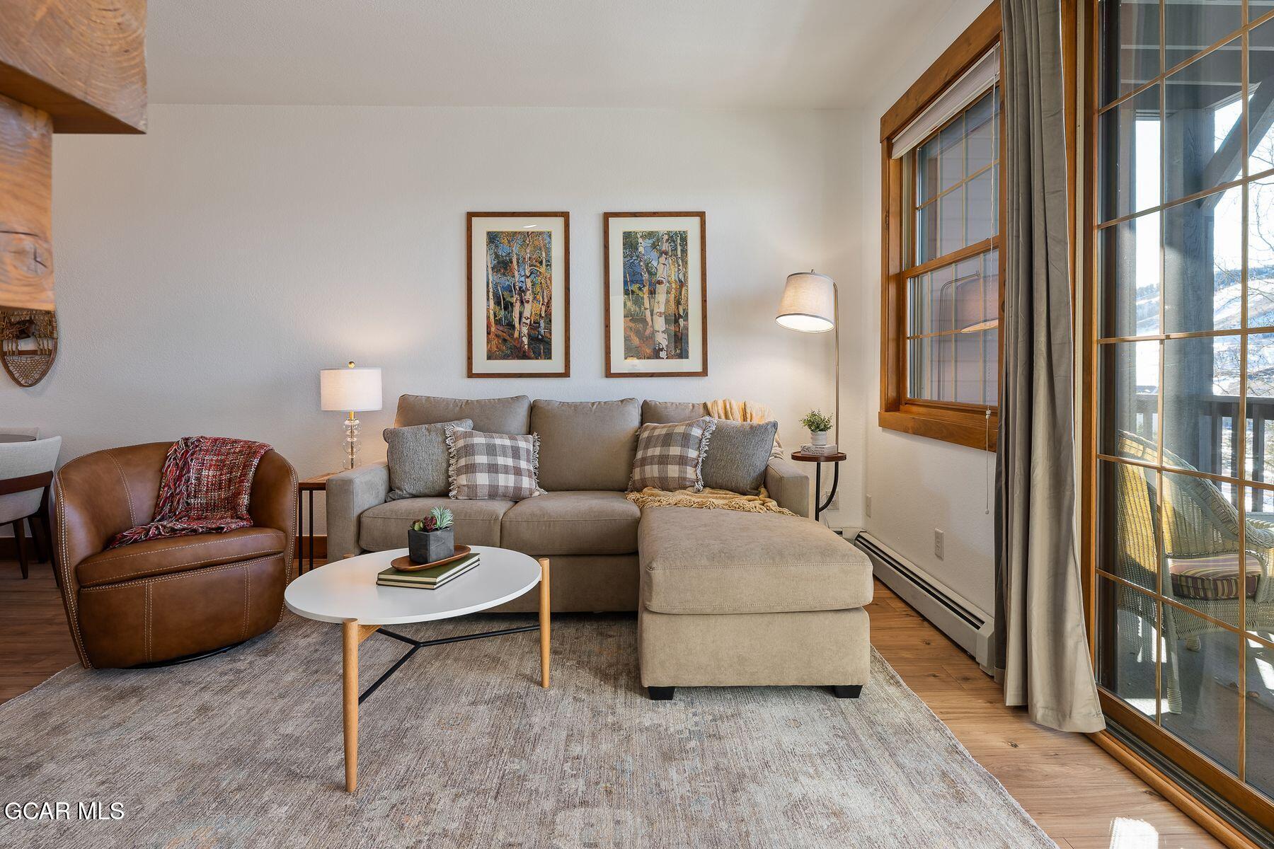 Living room with a gray sectional, leather armchair, and large wood-trimmed windows.